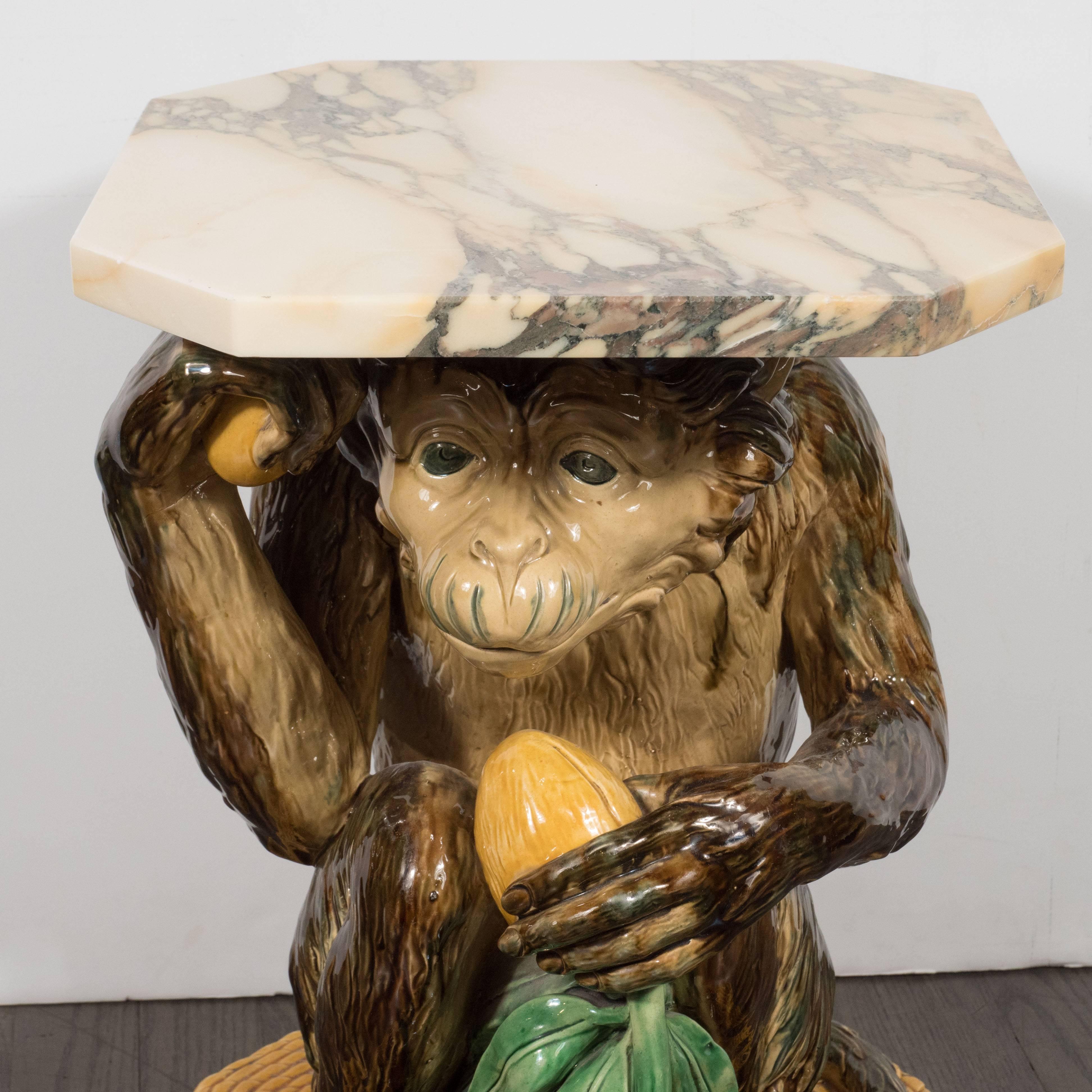 This whimsical occasional table was fabricated by Minton of England roughly 150 years ago. It features a crouching monkey holding a mango in each hand. The oblong piece of citrine skinned fruit in his left hand includes long emerald colored leaves