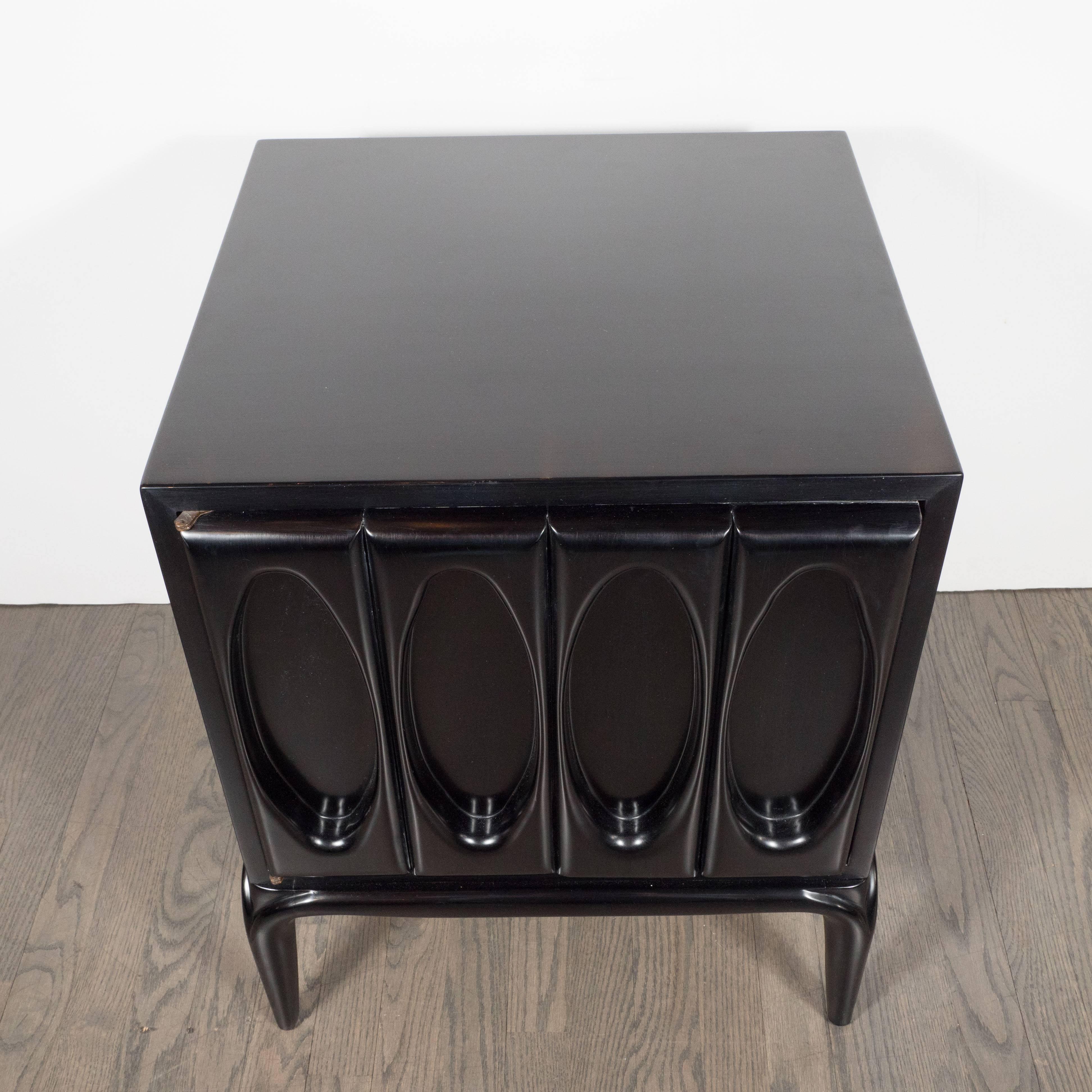 This sophisticated pair of ebonized walnut end tables or nightstands feature four rectangular panels with ovoid shaped cut-outs, tapered conical legs, and an interior cabinet with one glass shelf. This pair is the embodiment of simple elegance: