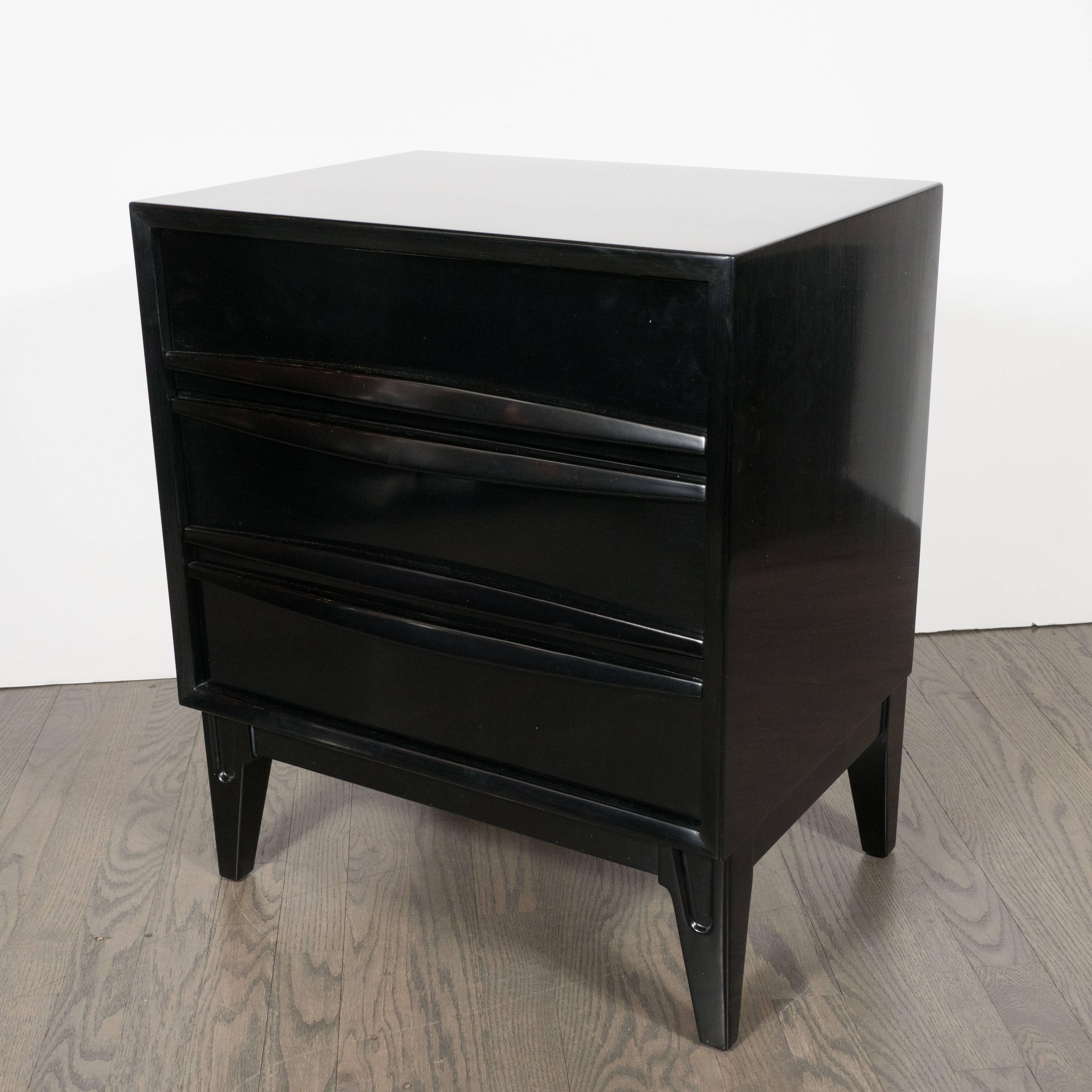 This elegant pair of nightstands were realized in the United States, circa 1960. Each features gently tapered legs, raised horizontal slat pulls that resemble two pairs of abstracted and stylized lips when closed, plus three commodious drawers