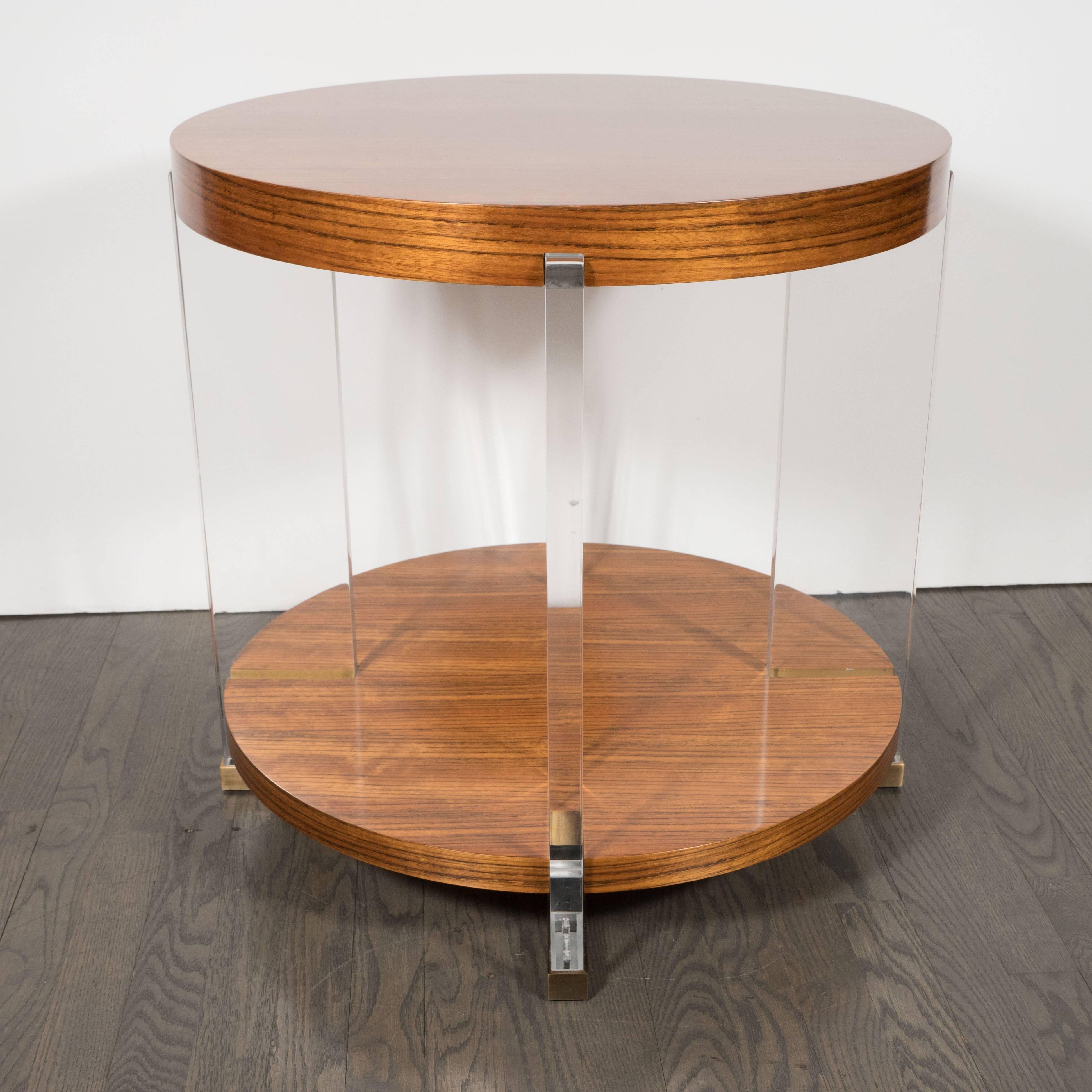 This chic tables feature translucent Lucite supports, brushed brass feet, and two tiers of book-matched Mozambique, whose high-key contrasting grain appears like tiger's eye gemstones. With its austere geometric forms and luxe exotic wood juxtaposed