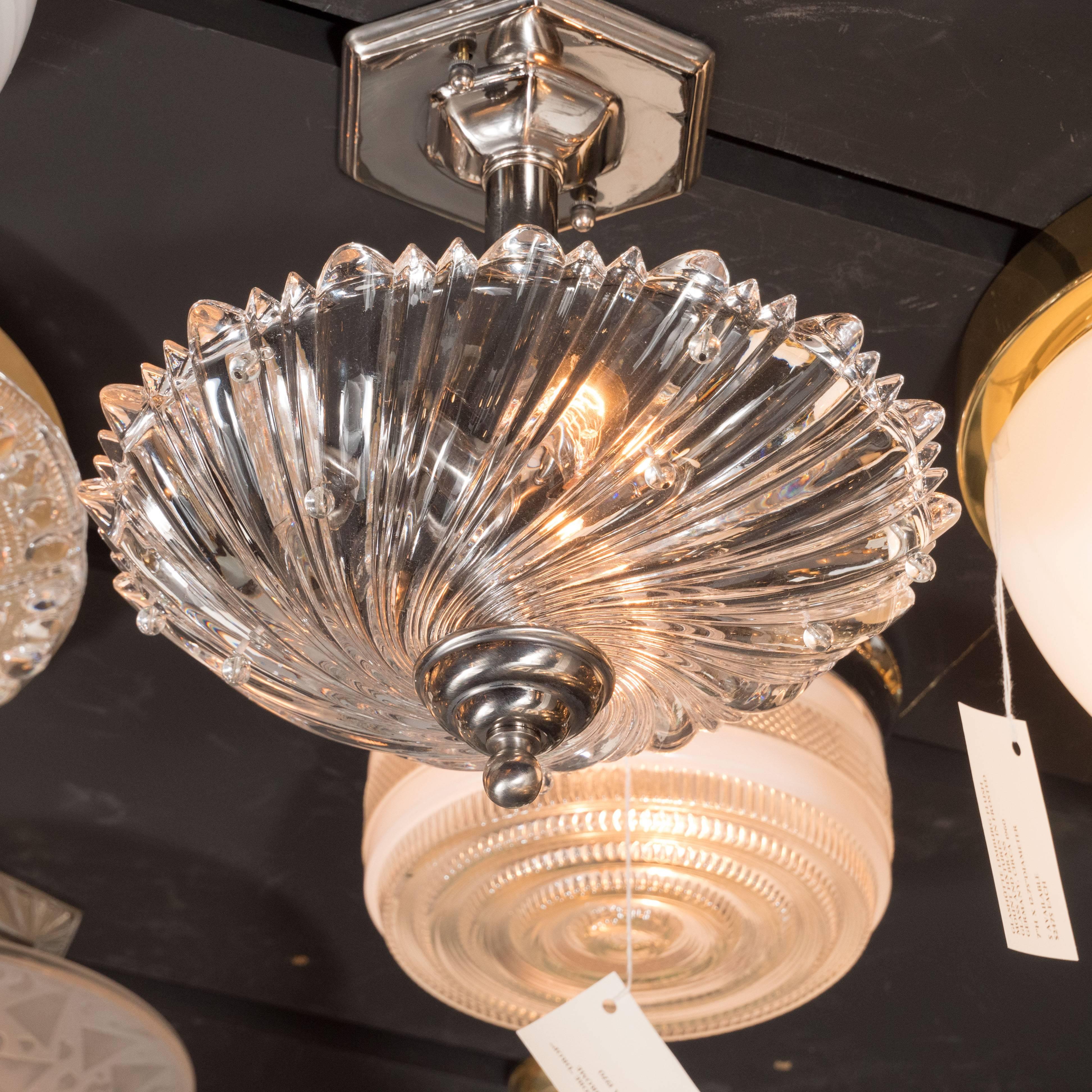 This modernist semi-flush mount features a dynamic whirlpool design in translucent glass with round glass bead embellishments protruding from the heavily textured surface. The fixture attaches to a skyscraper style octagonal base in polished nickel