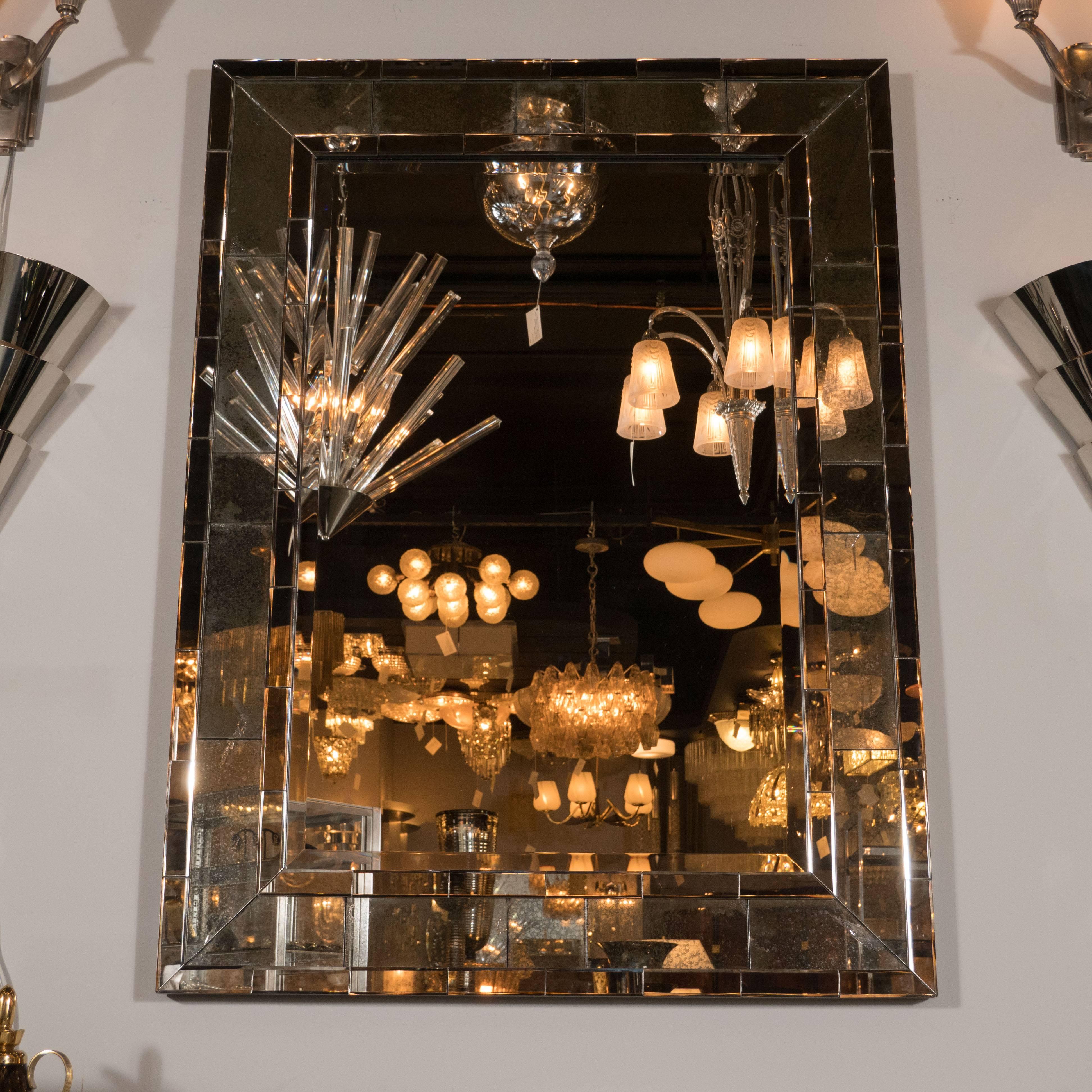 This elegant Mid-Century Modernist mirror features a mosaic antiqued mirror border with a beautiful patina. The contrast between the radiant center and the smoky organic texture of the antiqued mirror offers a truly stunning contrast, which adds