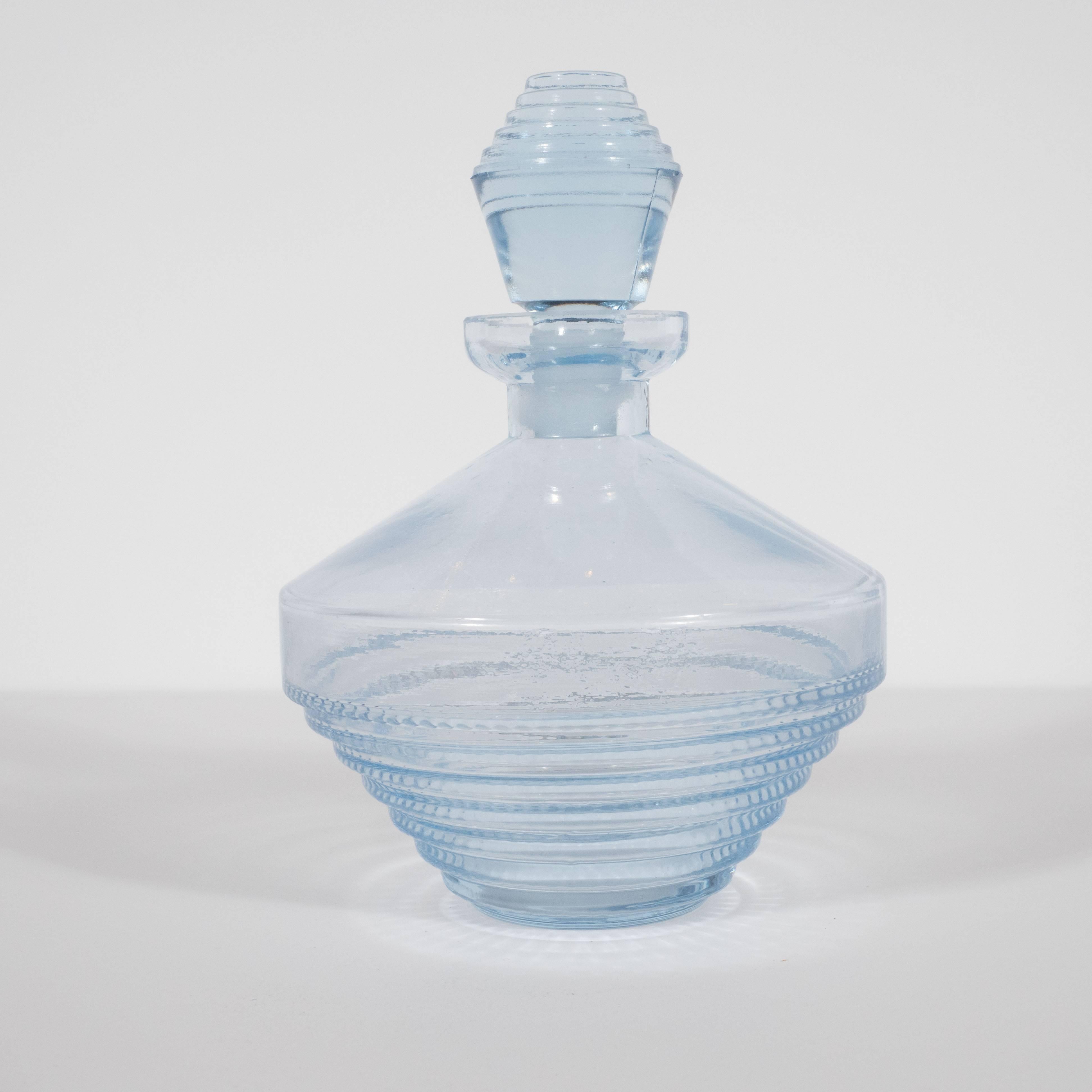 This lovely cornflower blue perfume bottle features a skyscraper style base consisting of graduating tiers of stepped glass with a subtle rippled pattern on the bottom of each tier. They culminate in a central band that circumscribes the centre of
