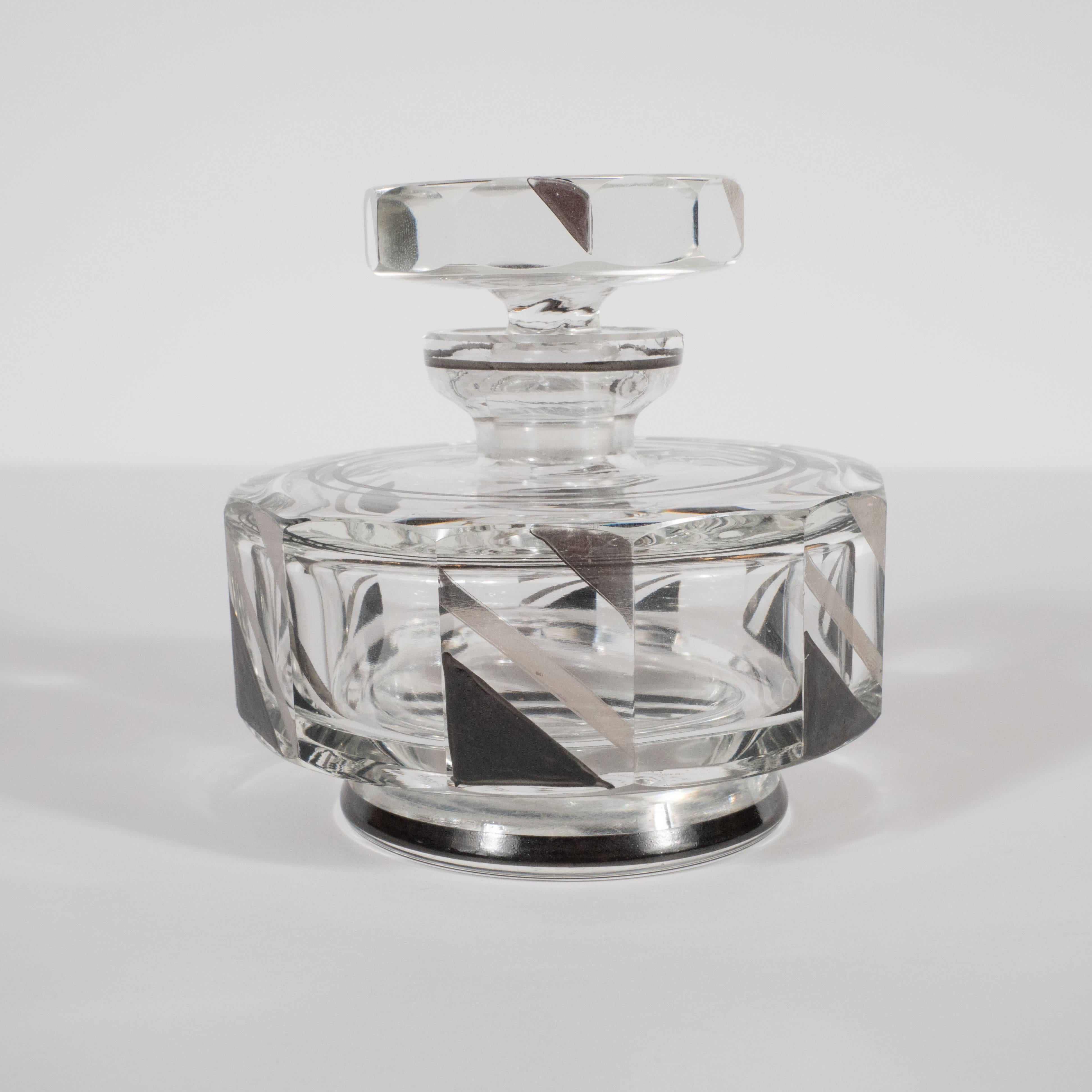 This refined Czech perfume bottles is composed of a beveled circular form (ten faceted sides in all) as well as a stopper of the same shape. A geometric pattern adorns alternating panels of the bottle- consisting of a black enamel in the lower right