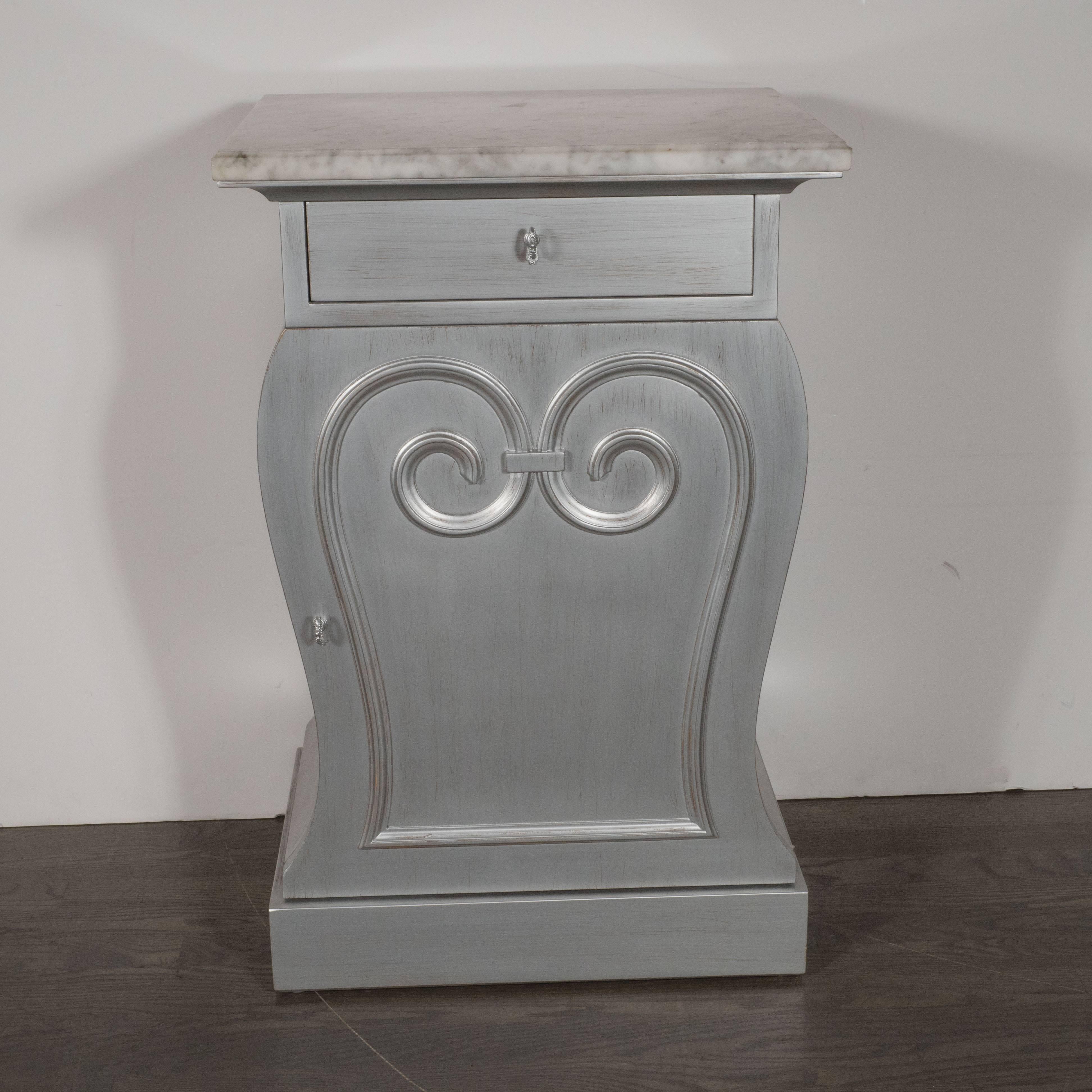 This gorgeous pair of Hollywood Art Deco end tables or nightstands was realized by the esteemed American producer Grosfeld House, circa 1945. They a raised scroll design in the center of each cabinet panel, which is repeated in the sinuous curves of