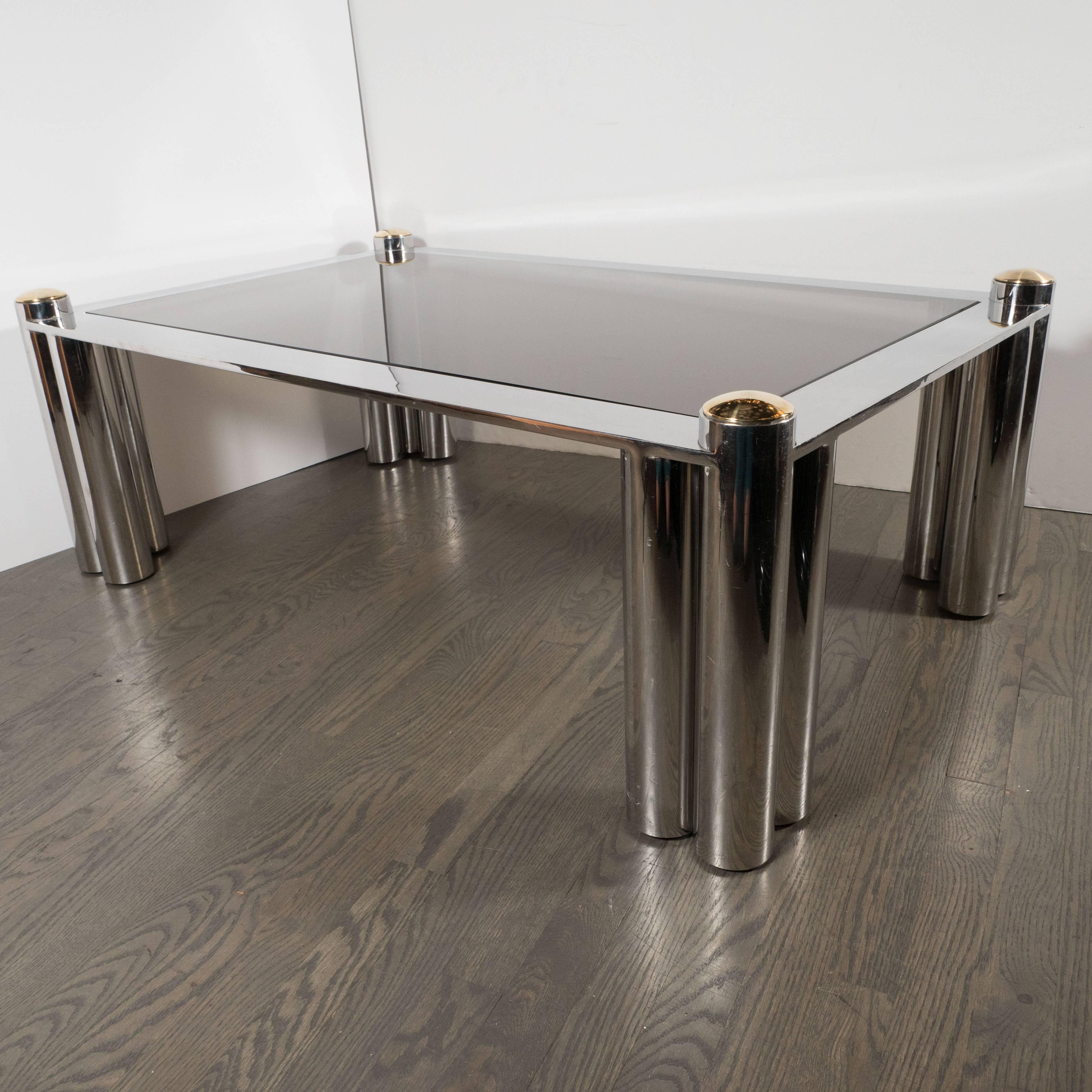 This handsome Mid-Century Modern cocktail table was engineered and crafted in America, circa 1970. It boasts the strong bold lines and Industrial materials that collectors of the period adore. With its flanked cylindrical legs, smoked glass top, and