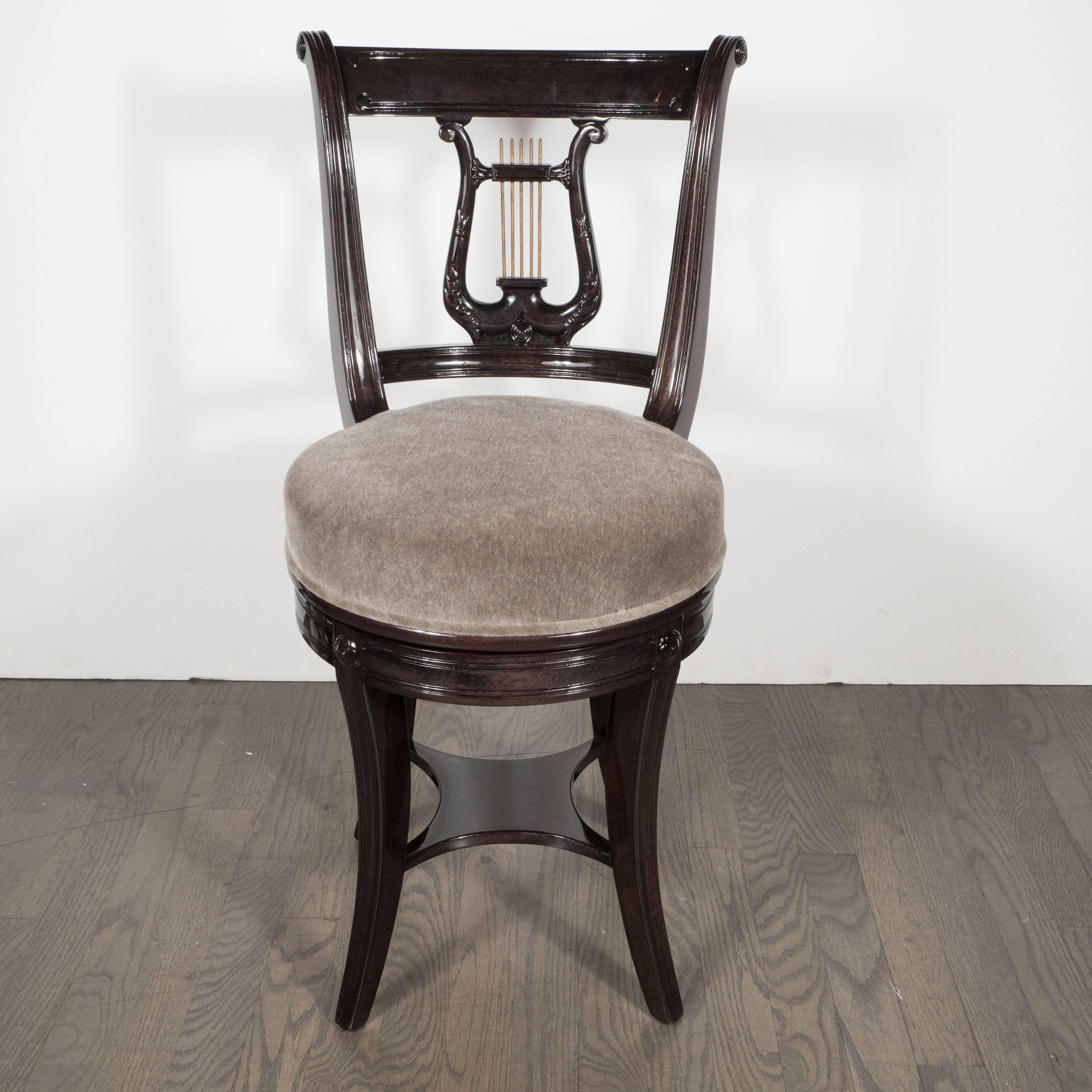 This whimsical stool or vanity chair was realized in America, circa 1940. A stylized lyre, with brass spindles, forms the back of the chair. The apron that supports the dove gray mohair seat features stylized floral details and a reeded design. This