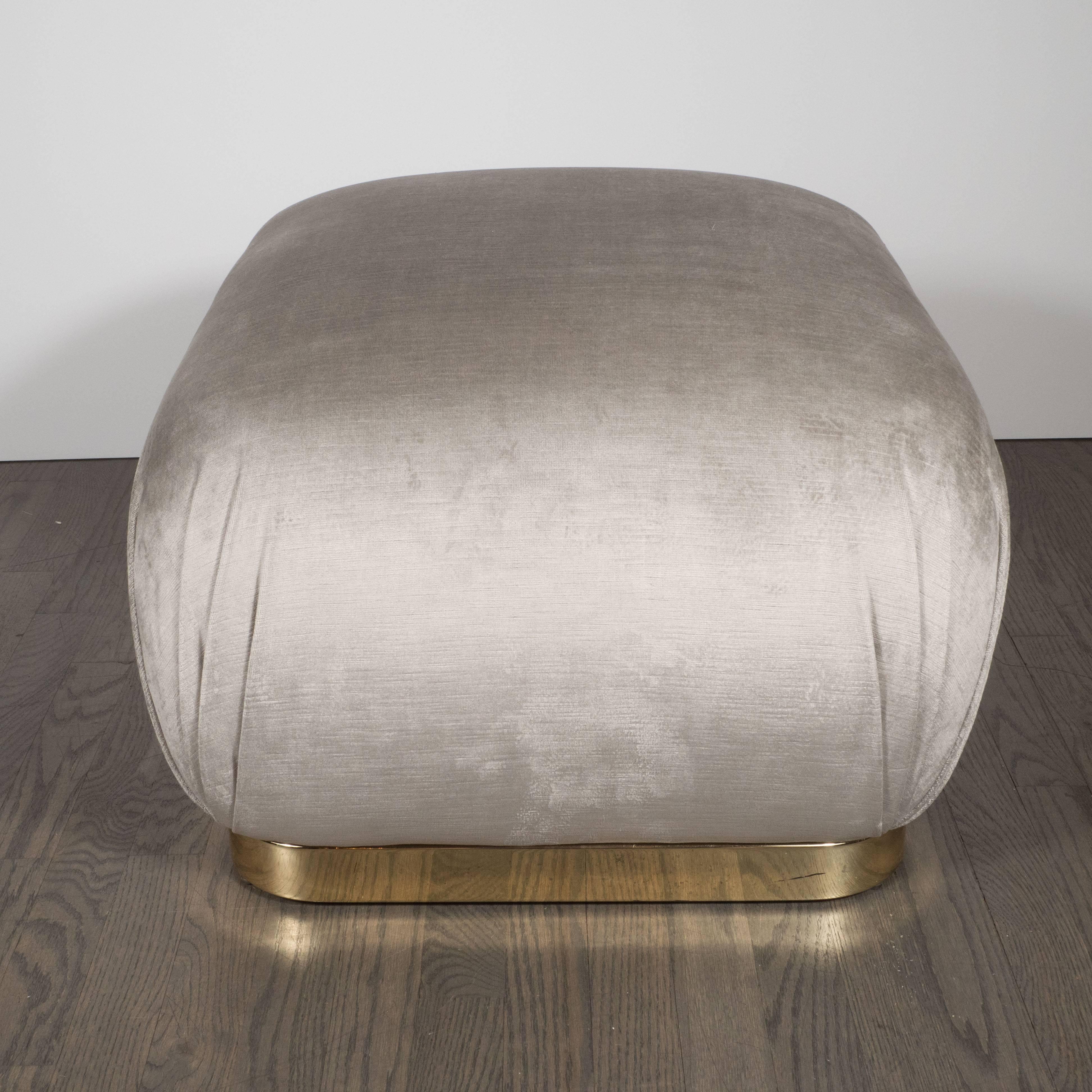 These sophisticated Mid-Century Modernist soufflé poufs, realized in the manner of Karl Springer, feature a lustrous square brass bases with rounded edges and platinum velvet upholstery. With their austere lines and luxe materials, these pieces