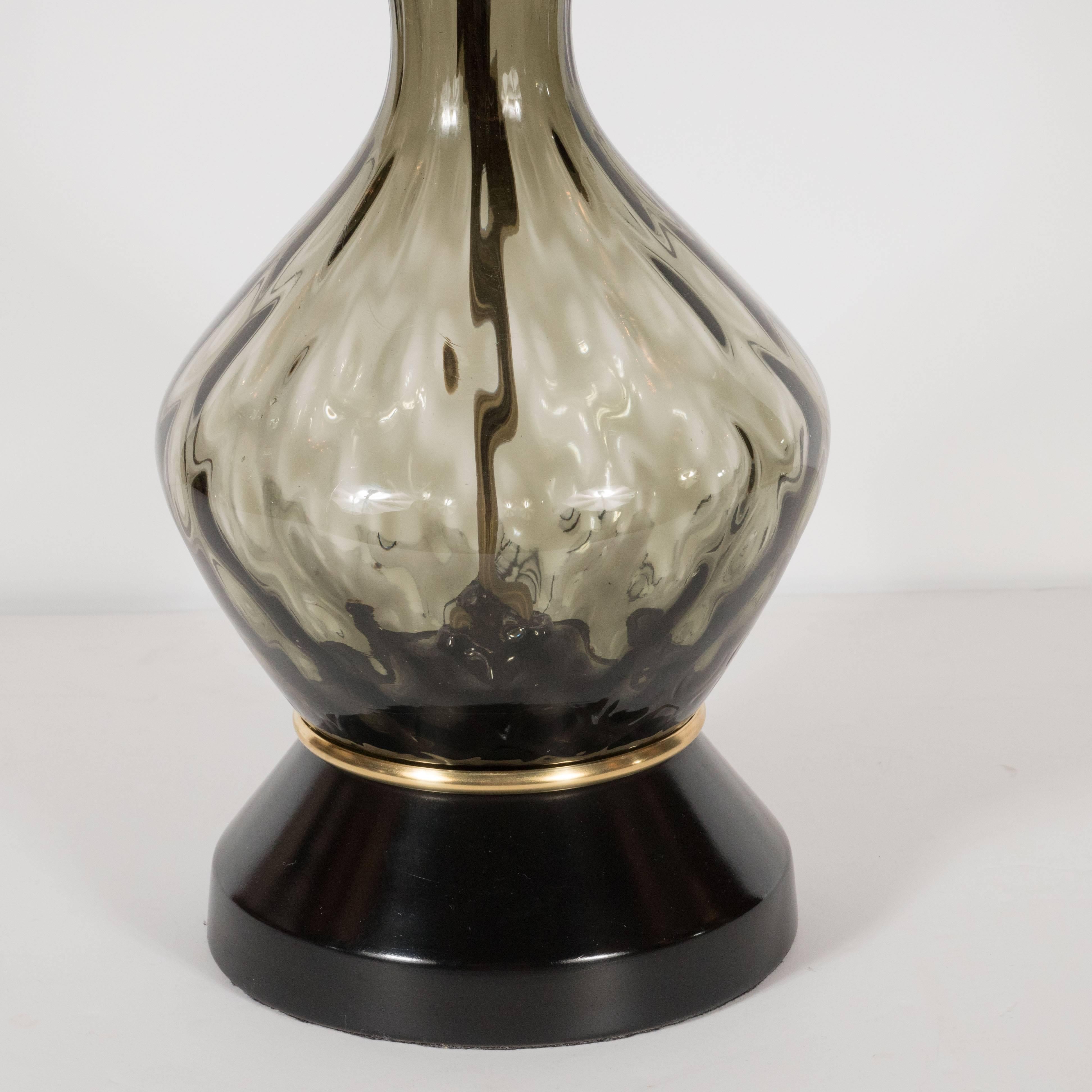 This sophisticated pair of Mid-Century Modern handblown table lamps were realized in Murano, Italy- the Venetian island renowned for producing some of the highest quality glass for centuries, circa 1960. These pieces feature round black enamel bases
