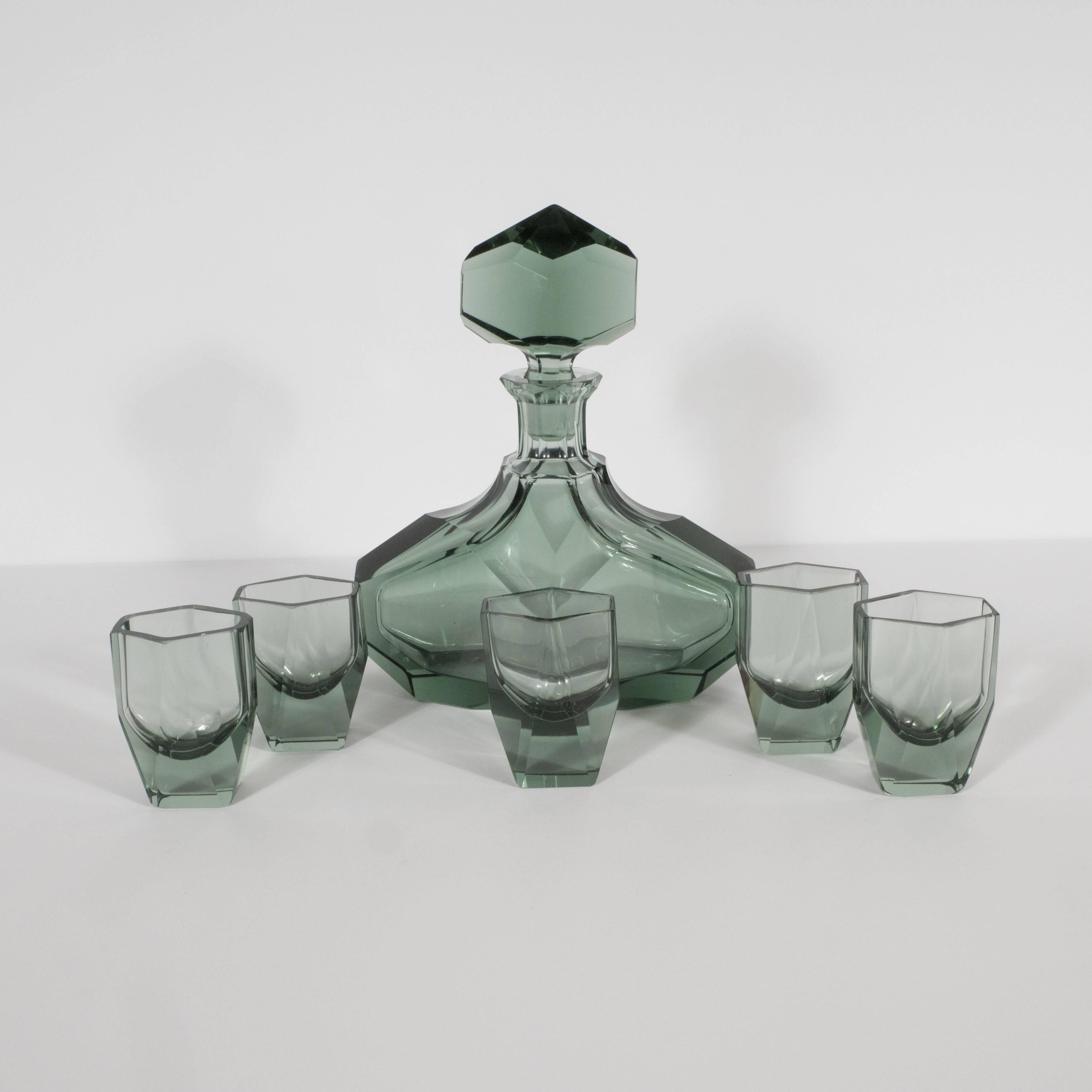 This elegant Art Deco bar set, realized in France, circa 1930, features a decanter and four hexagonal shot glasses in a smoked Alexandrite hue (a dark blue-green). All of the pieces feature beveled sides creating a wealth of geometric forms within.
