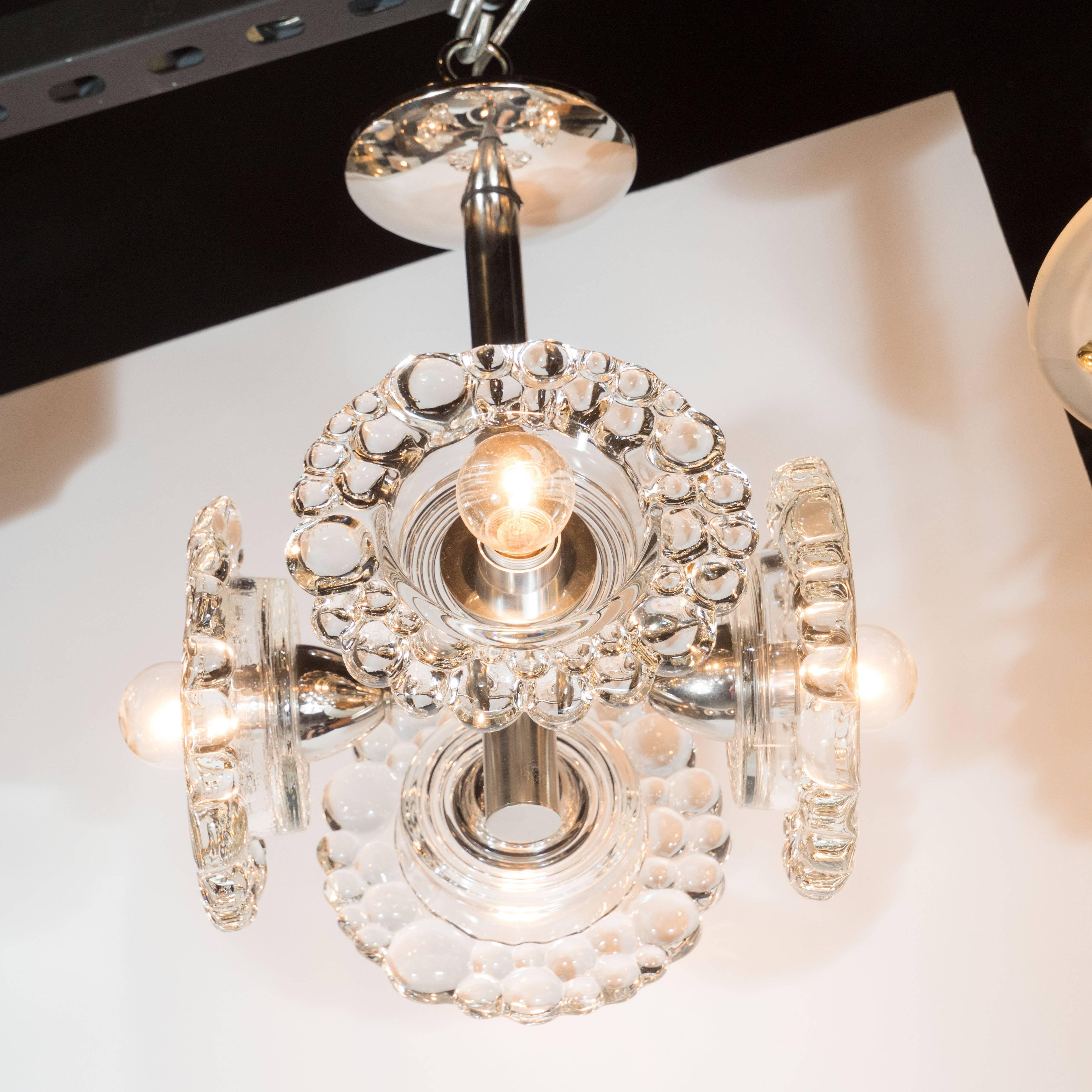 This sophisticated Mid-Century Modern chandelier was realized by the esteemed Austrian glass studio J.T. Kalmar, circa 1960. It features four straight cylindrical arms extending perpendicularly from a two-tiered cylindrical chrome body. The