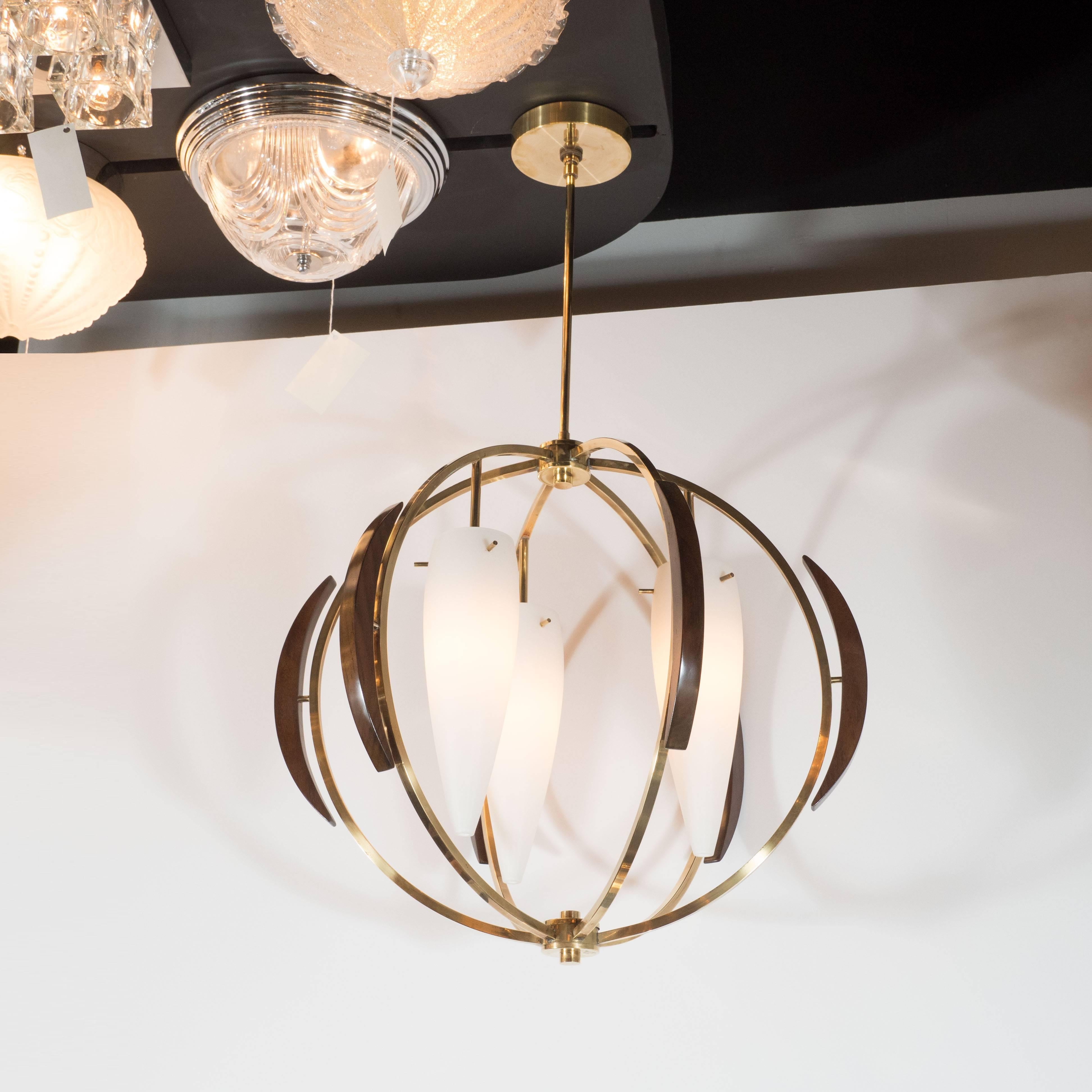 This sophisticated globe form chandelier was realized in France, circa 1950. It features six demilune brass arms, traced on the outside by crested forms in hand rubbed walnut, attached to the ceiling by a brass rod. Gently flared conical frosted