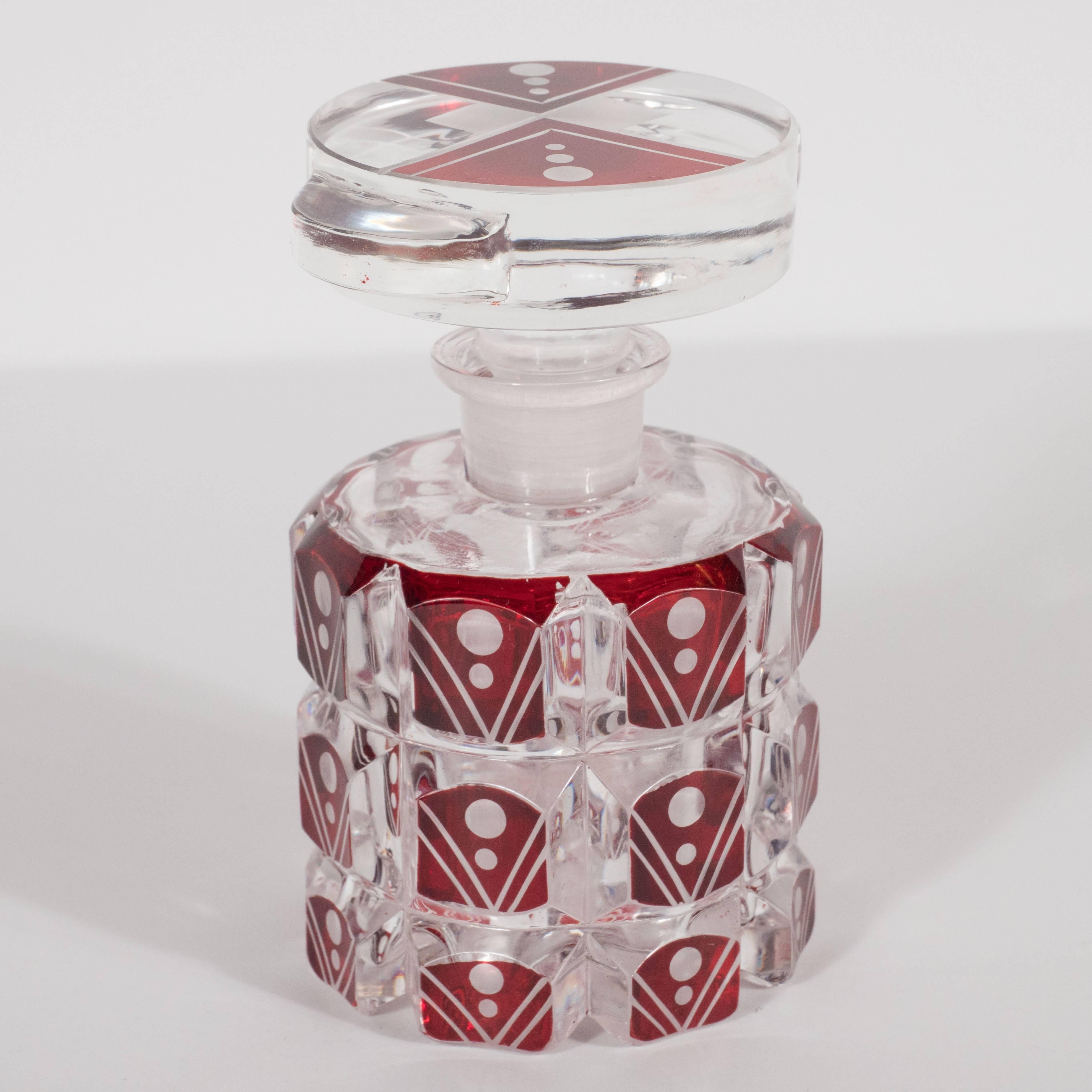 This exquisite cylindrical glass perfume bottom features rows raised and beveled rectangular forms in crimson glass circumscribing its body. On the face of each of these raised forms are chevron designs consisting of two parallel lines meeting in