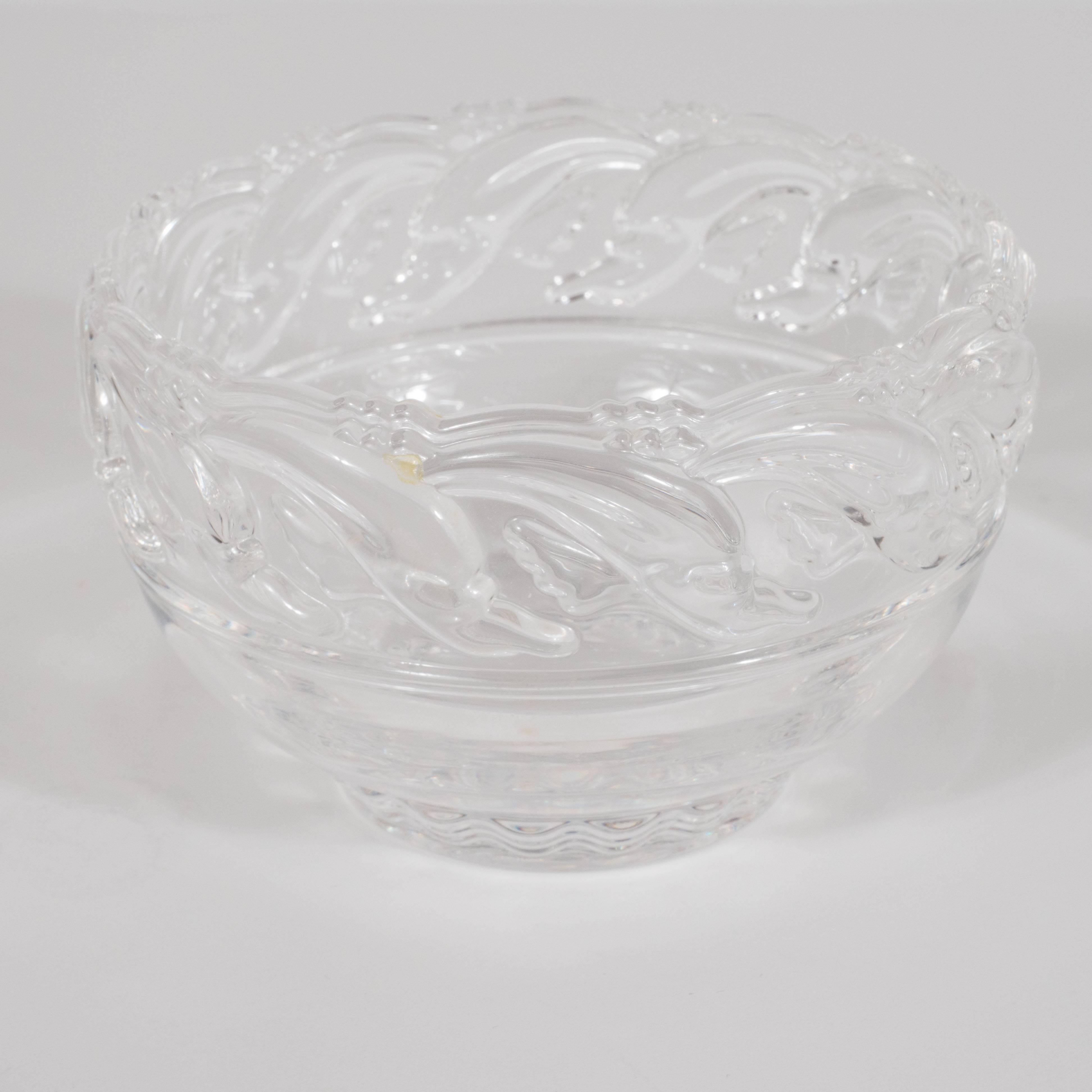 This charming and delightful glass bowl was realized by the renowned American design house, Tiffany & Co., circa 1980. It features stylized renditions of dolphins, in raised glass, riding the crests of waves on the upper portion of the bowl. While