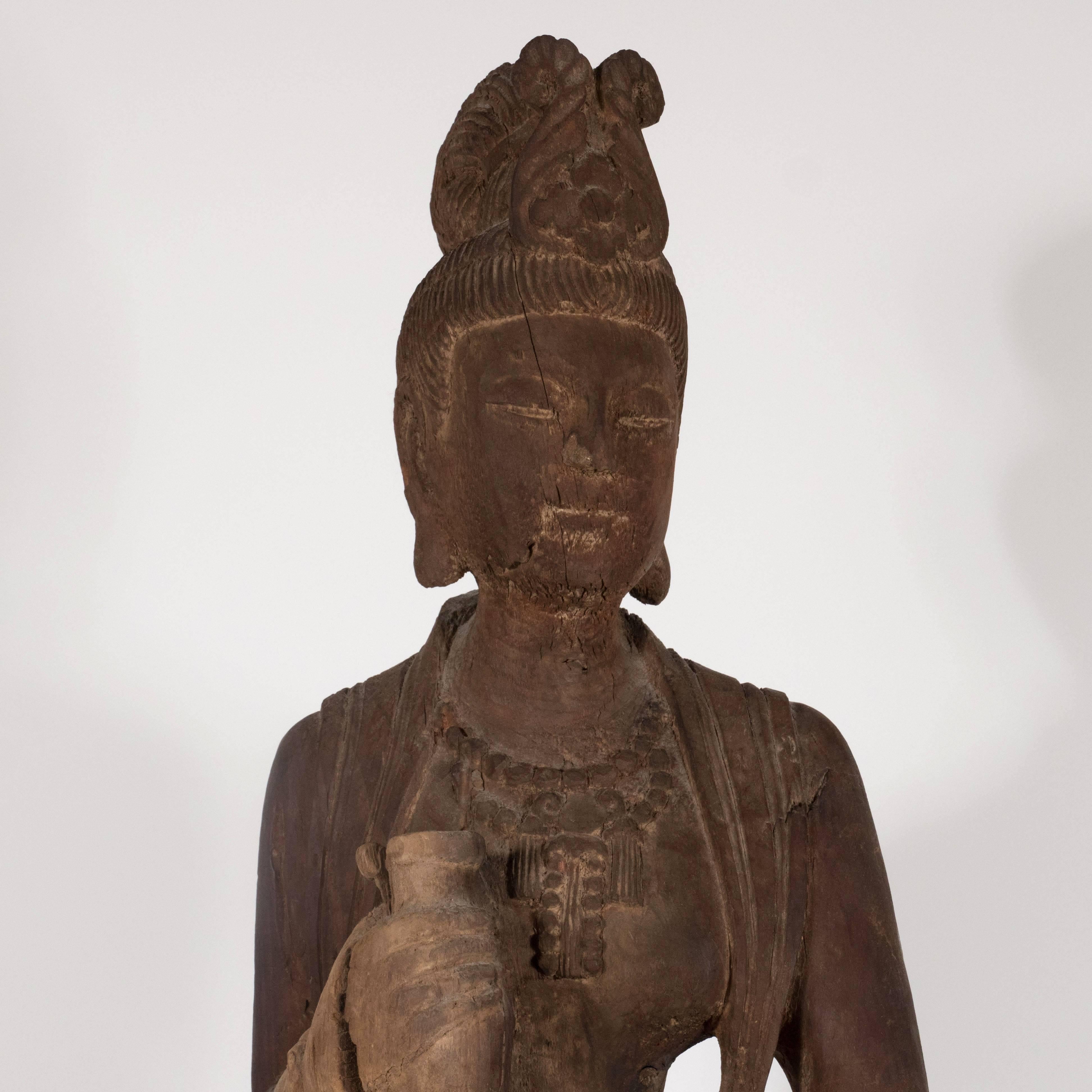 This beautiful sculpture realized in China in the 18th century depicts Guanyin, a Bodhisattva associated with compassion. The female form holds a pot in her hands. She appears draped in a long flowing dress with a tiara- the many details of her