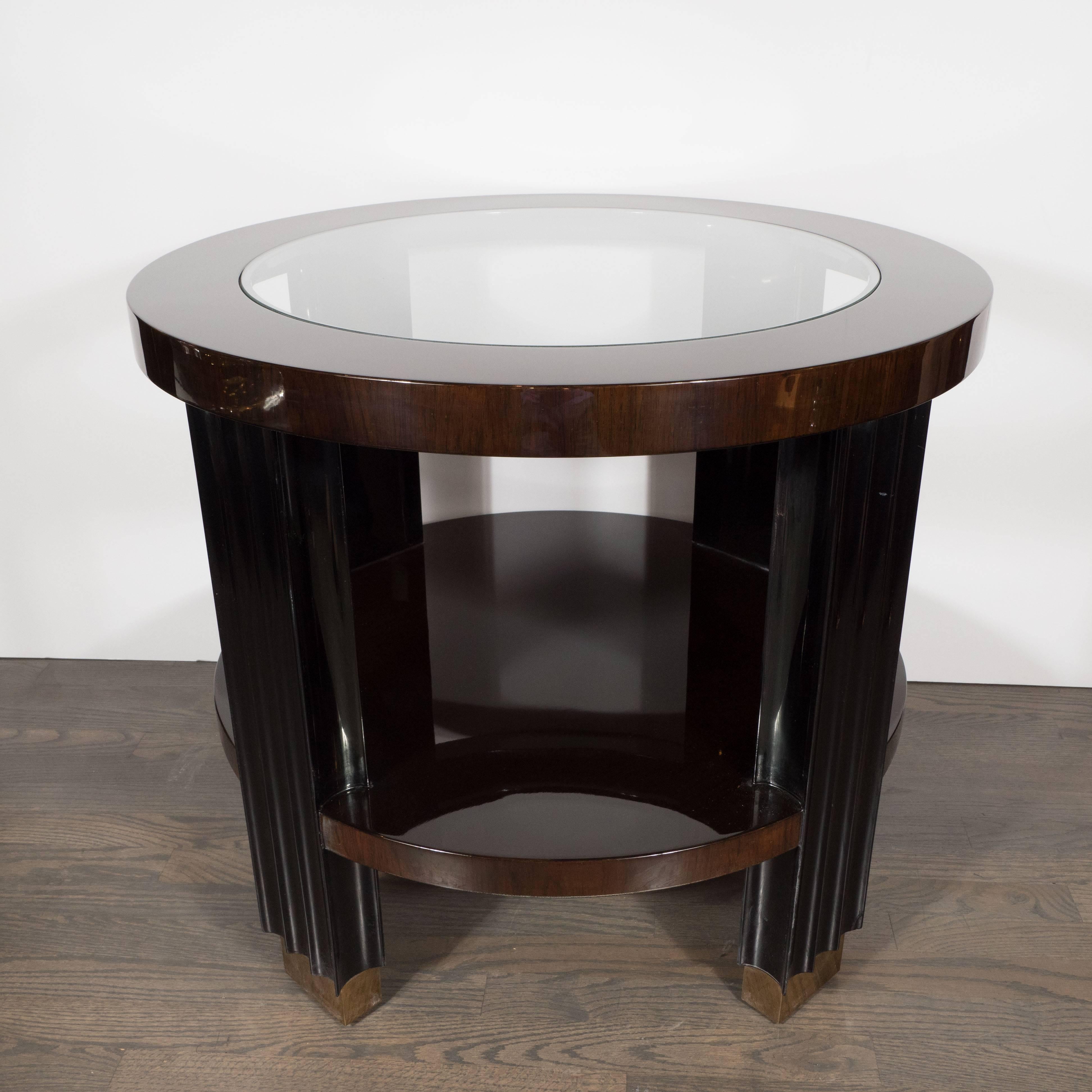This striking occasional table was realized in the United States towards the end of the 20th century, likely in the 1980s. It features two table tops made of walnut- the top one has a circular glass insert in the center. The table is supported by