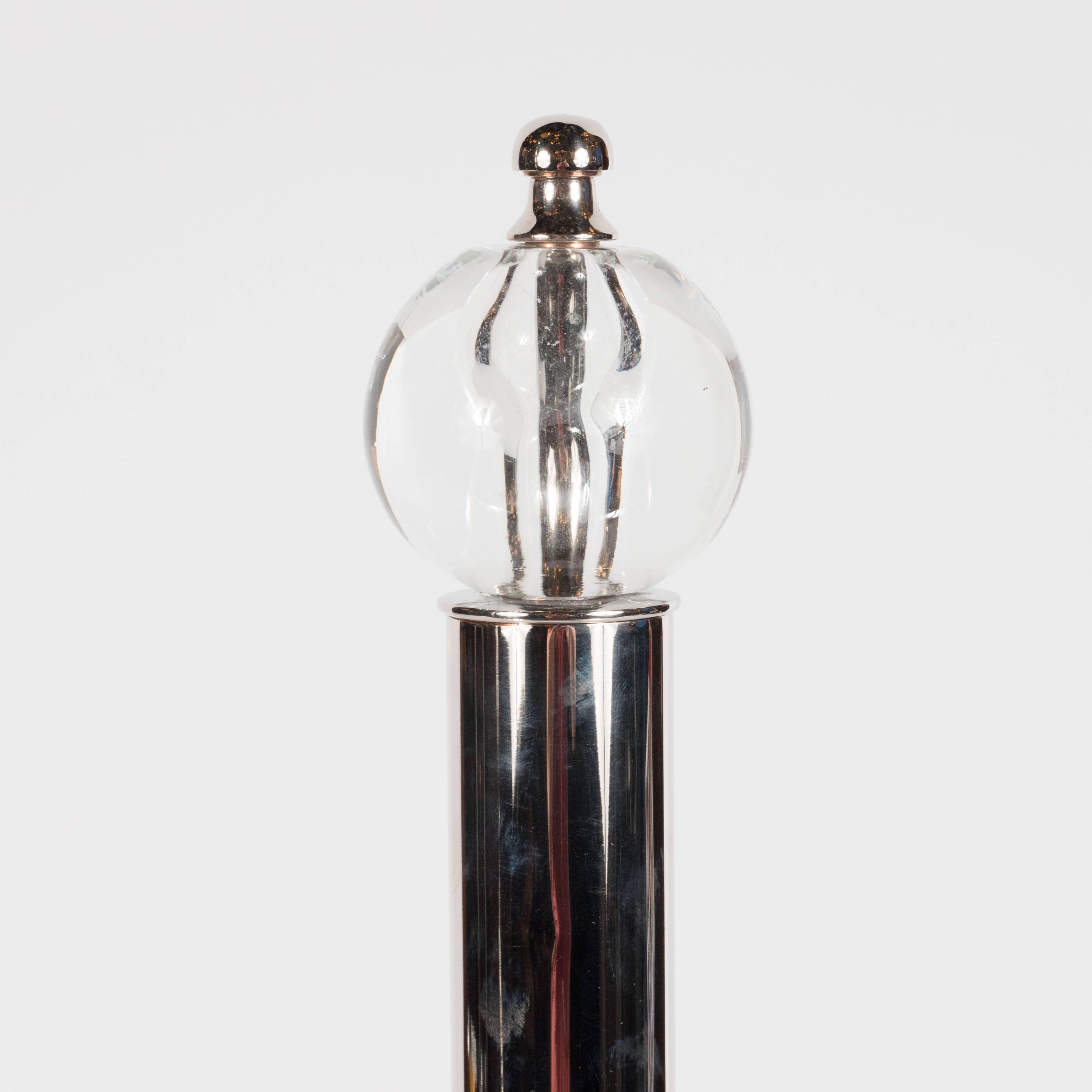This stunning set of machine age andirons was realized in the United States, circa 1935, in the manner of Donald Deskey. A cylindrical body in lustrous chrome ascends upwards from a square base (also in chrome). At its apex, a thin chrome rod
