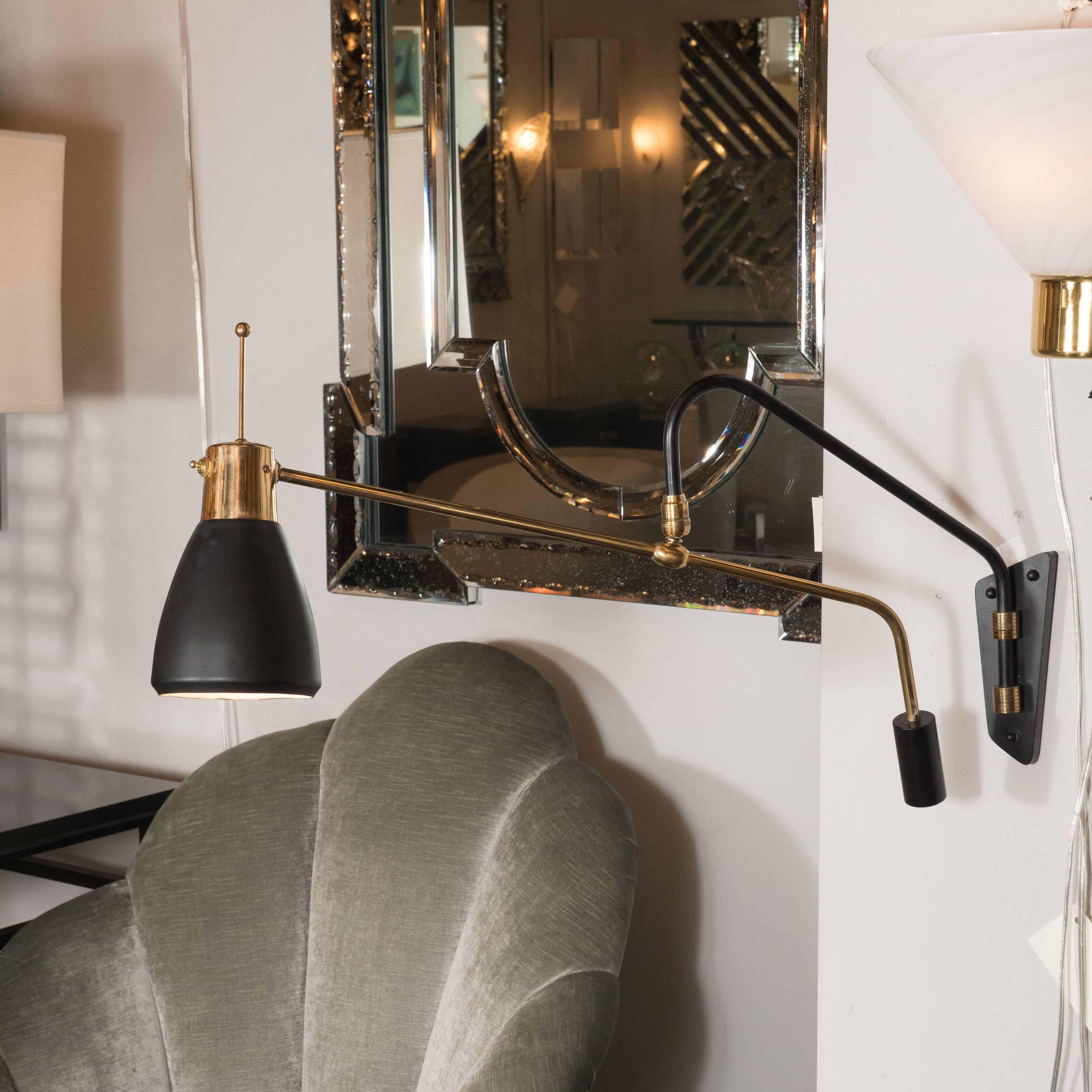 This stunning wall sconce, realized in Italy, circa 1950, offers a wealth of stunning contrasts in both materials and forms. A black arm curves upwards from an asymmetrically cut base in the same material, attached with brass cylindrical supports