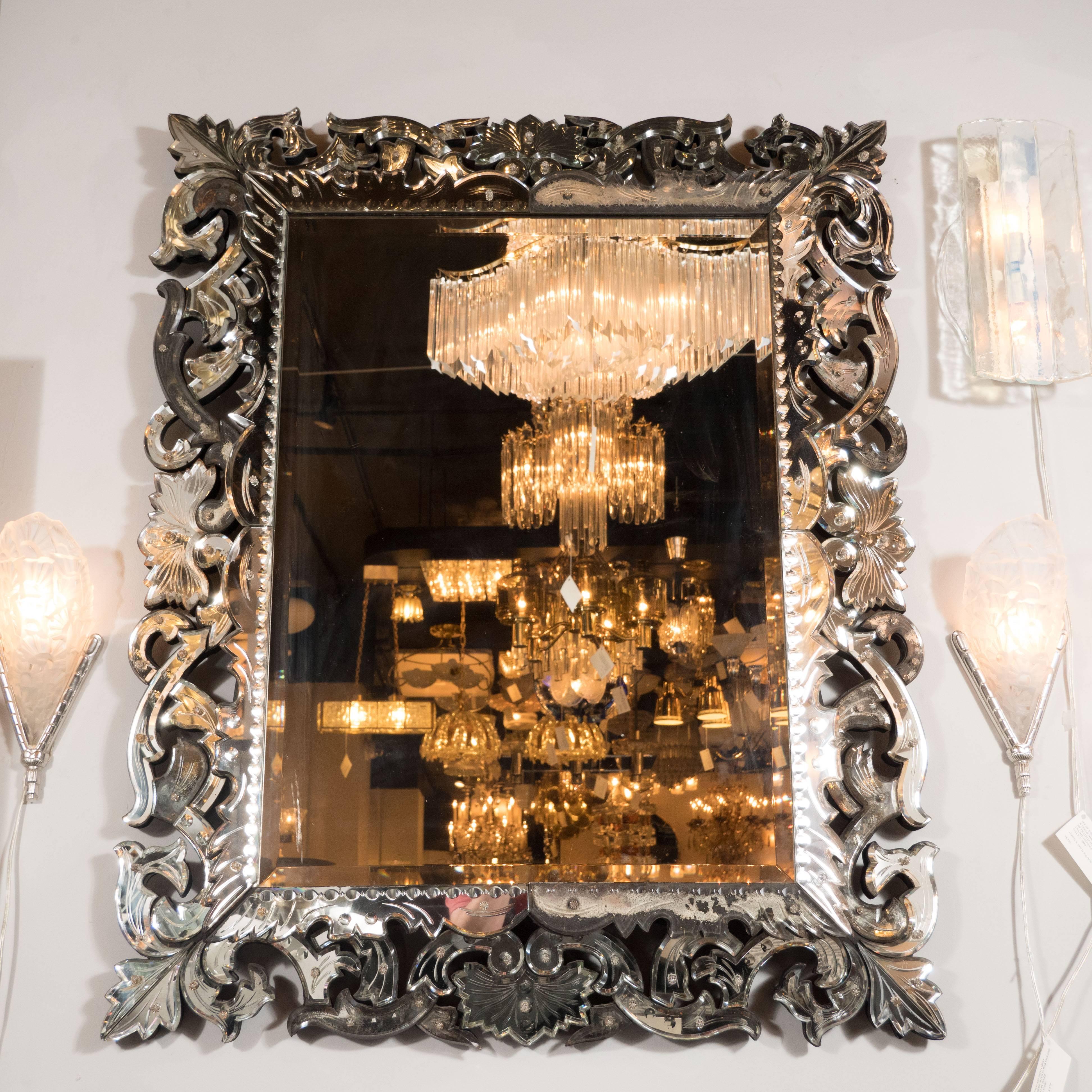 This stunning mirror was realized in France, circa 1925. It features chain beveling around the perimeter, and a stylized flame motif consisting of an abundance of abstracted forms cut from mirrored glass emanating from the square center. There is a