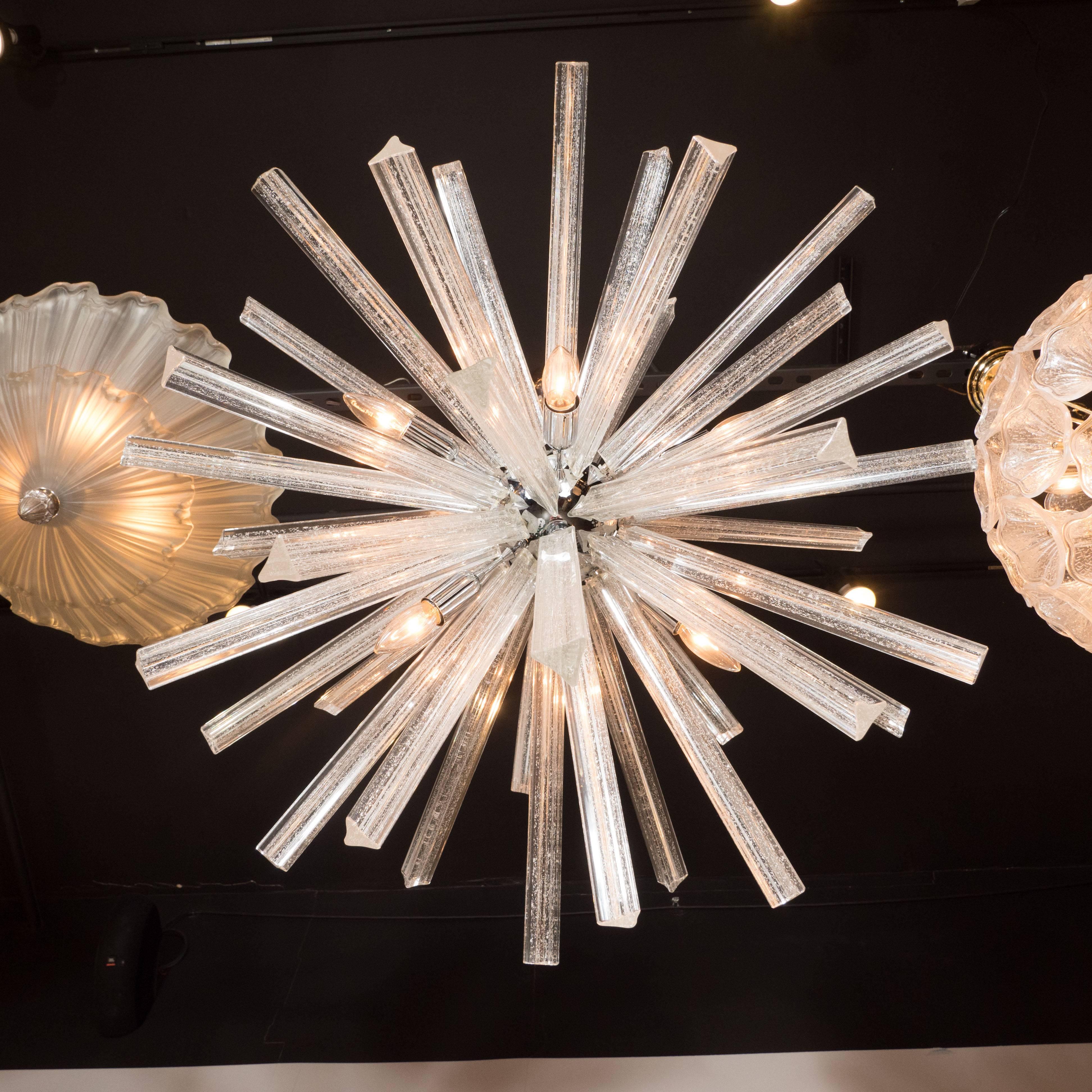 Dieser exquisite Sputnik-Kronleuchter aus mundgeblasenem Muranoglas bietet eine Fülle von Triedre-Kristallen - jedes mit einer Fülle von 24-Karat-Weißgold-Flecken -, die von einer zentralen Kugel aus glänzendem Chrom ausgehen. Der Baldachin und die
