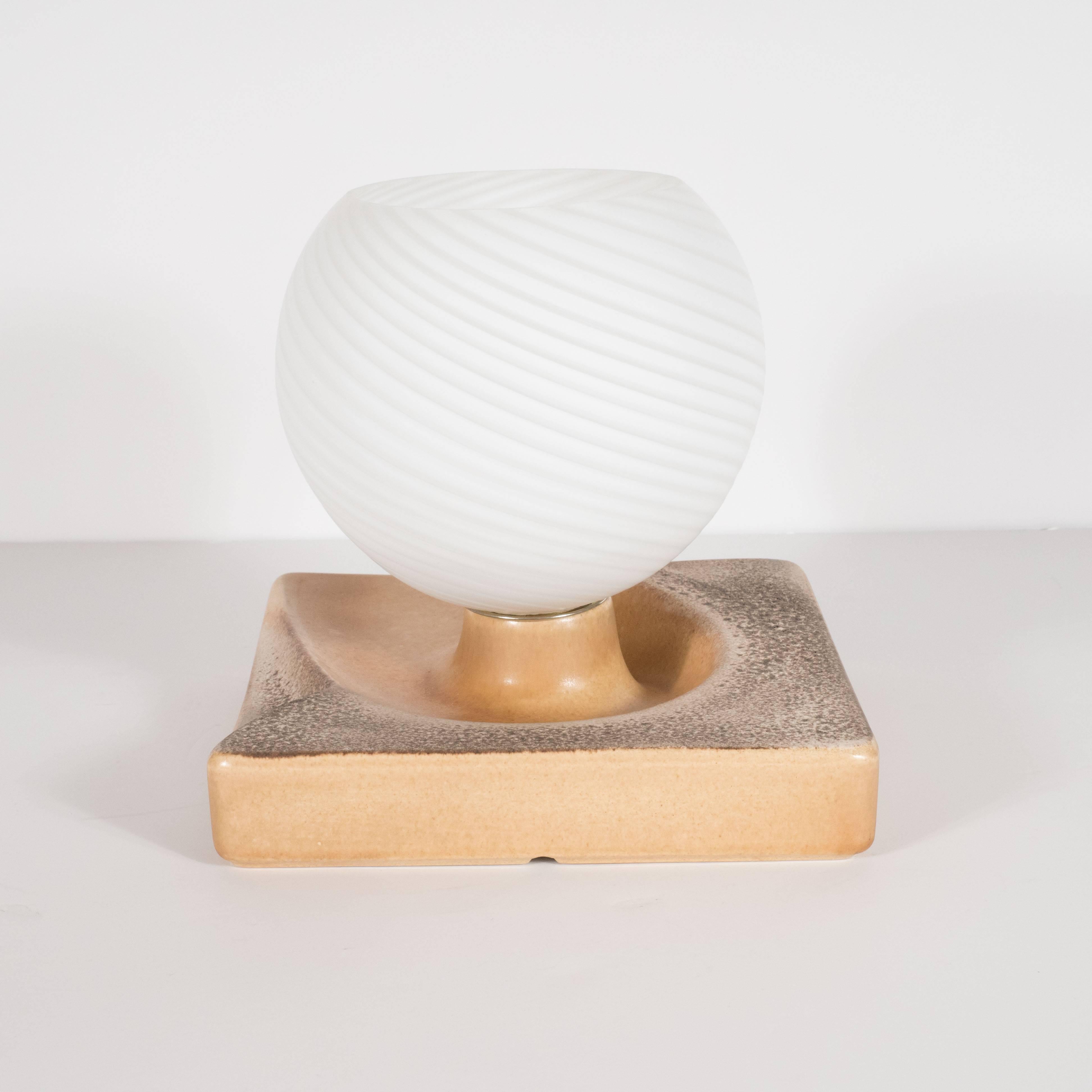 Replete with earth tones and a stunning crème brûlée glazed ceramic, this rare uplight was realized in Germany, circa 1960. It is an excellent example of the time and place. Its square body offers gentle curving contours that have a nearly