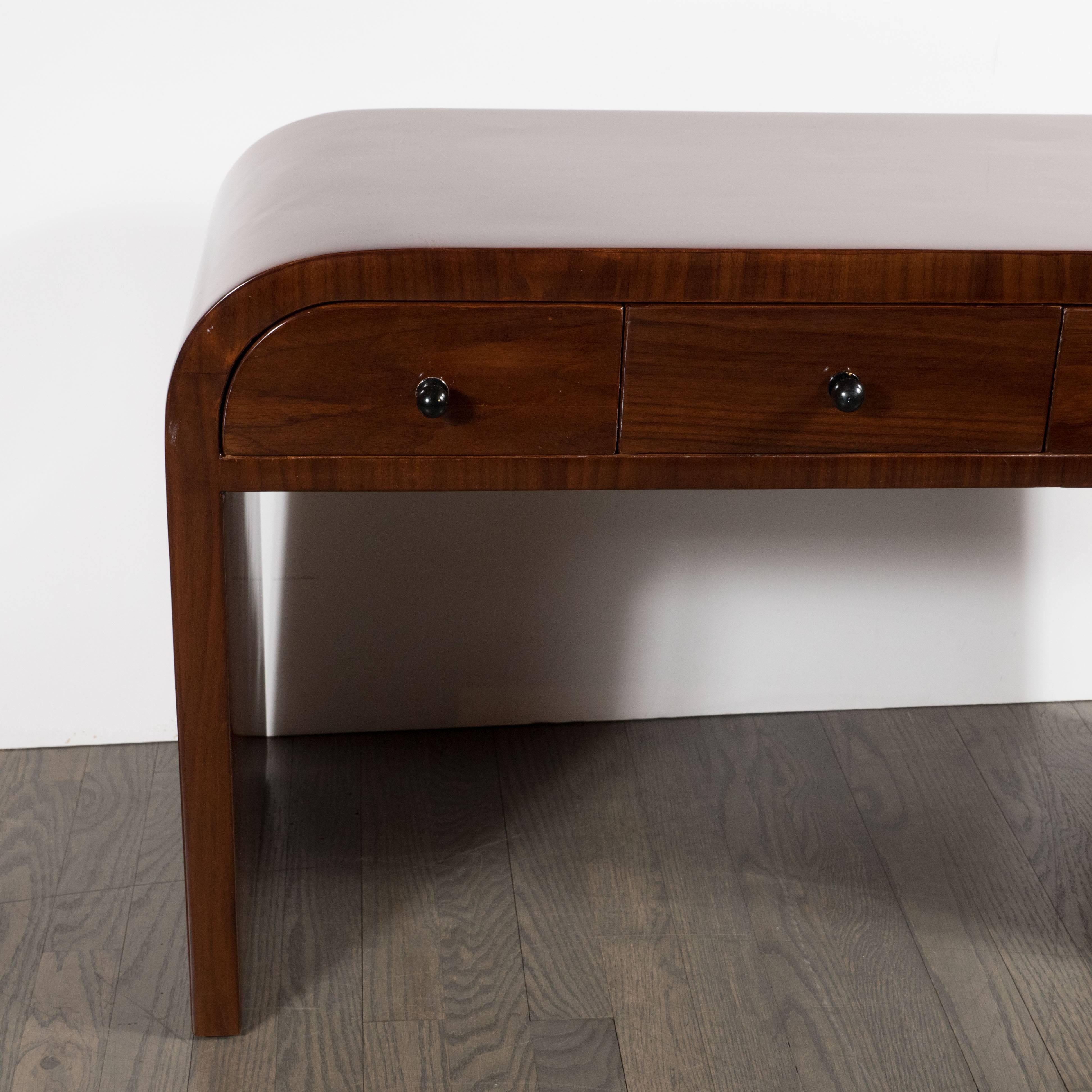 This refined pair of Art Deco end tables or nightstands were realized in the United States, circa 1935. They are an exceptional example of the time and place. They offer streamlined bodies, with elegantly sloping sides, and three drawers each with