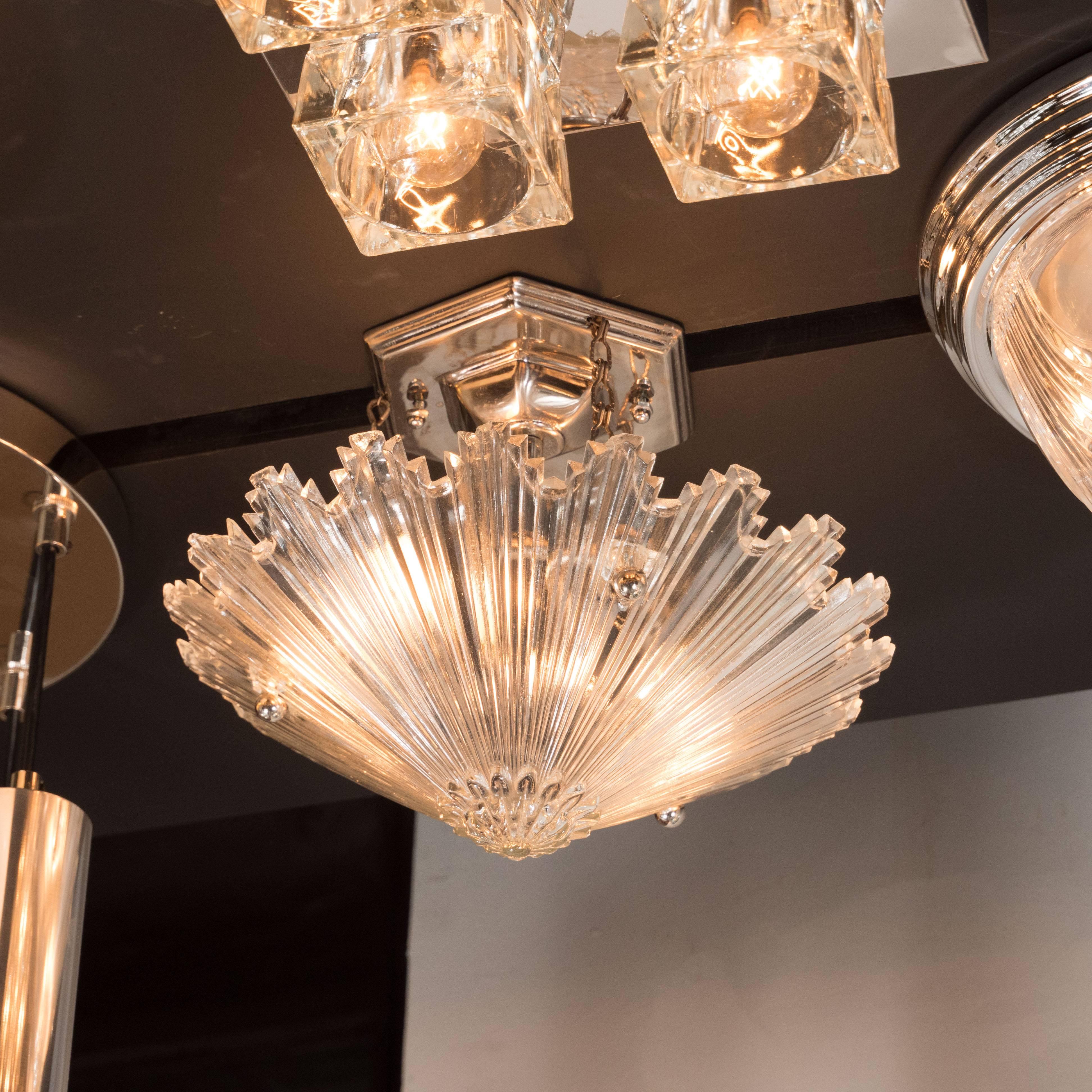 This stunning chandelier, realized in the United States circa 1935, represents America Deco Style at its finest. It offers a sunburst explosion of striated rays emanating from a round finial surrounded by petal-like embellishments. The staggered