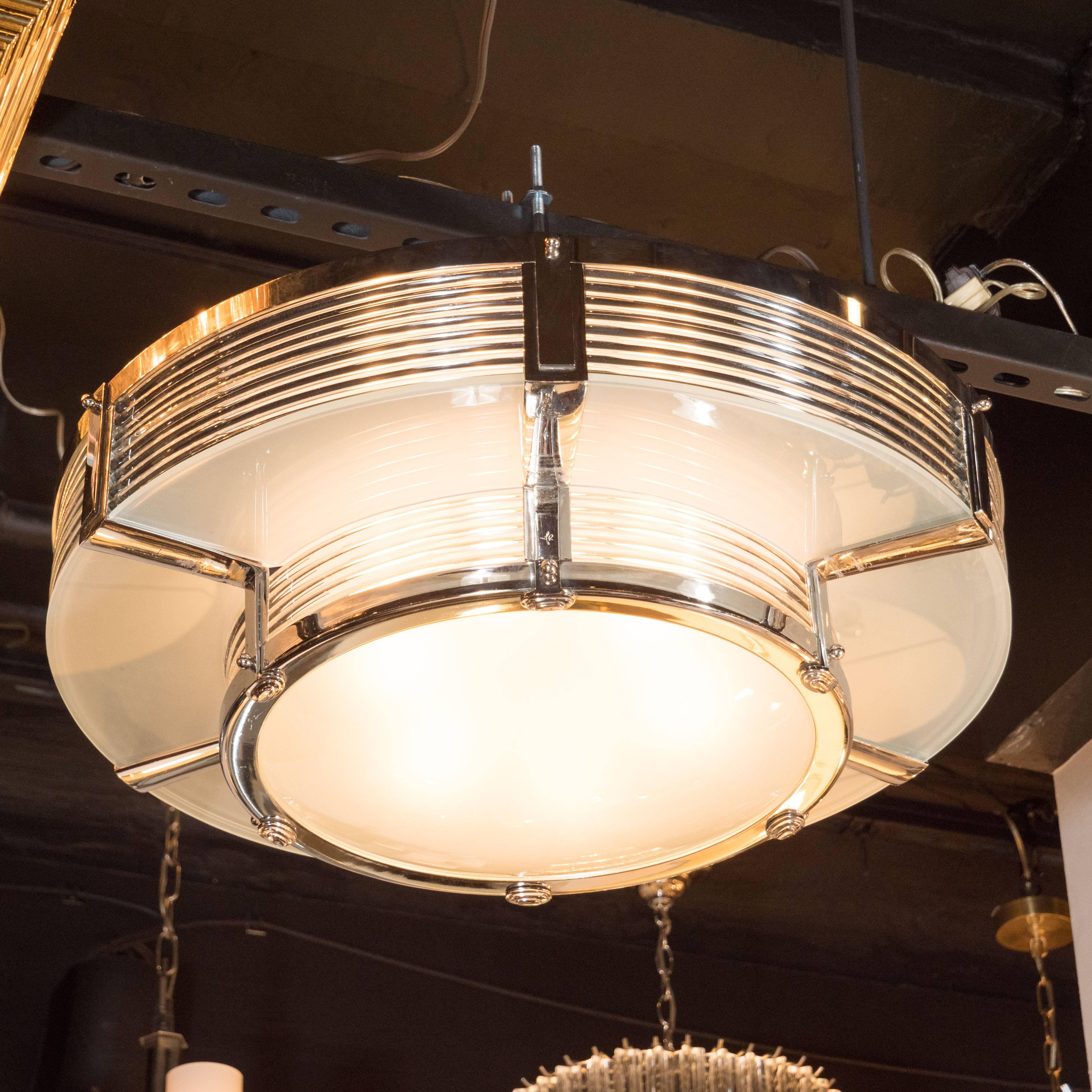 This sophisticated chandelier was realized in France, in the manner of Atelier Petitot. It offers the machine age details and clean, streamlined design that enthusiasts of fine Art deco design adore. It consists of two tiers with frosted glass