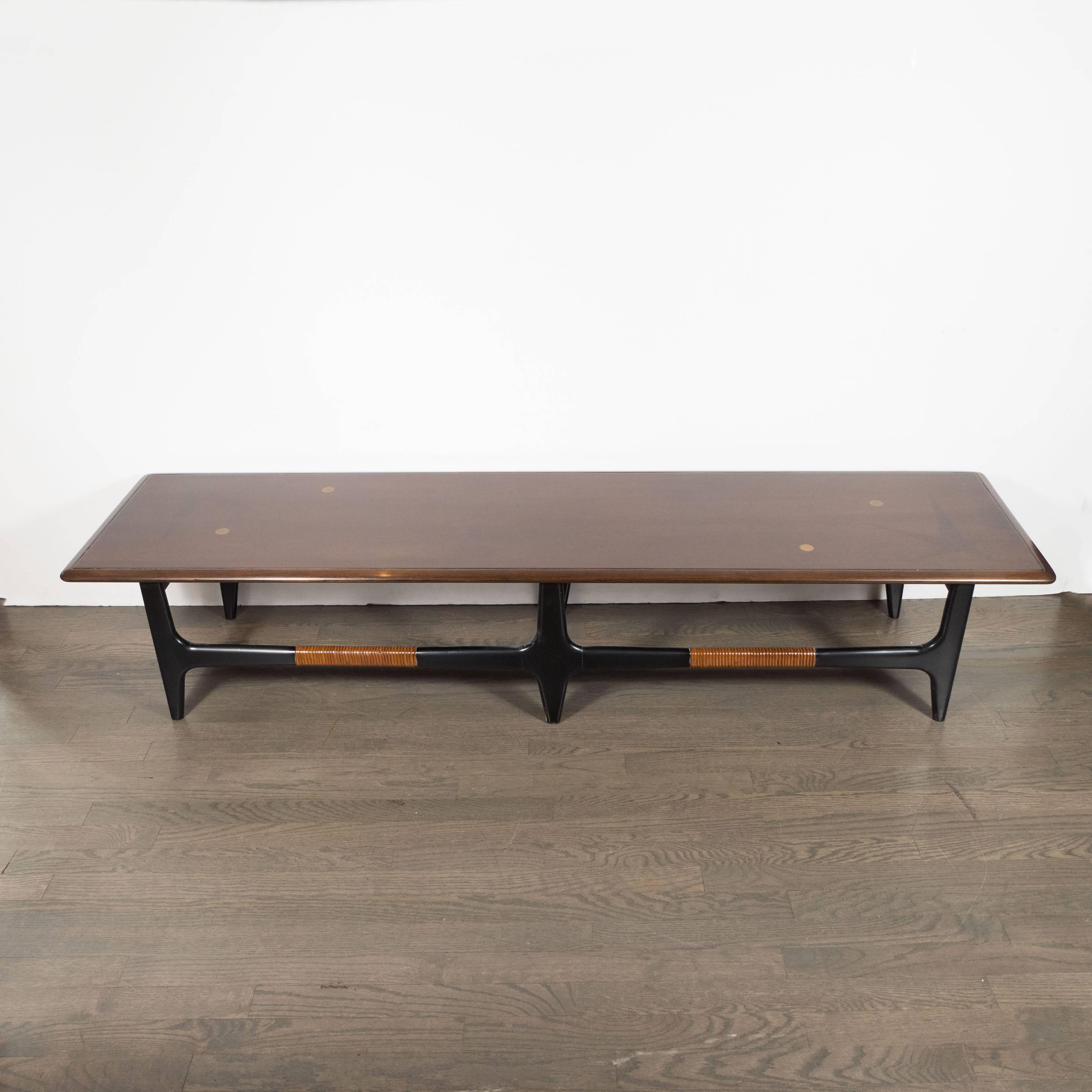This exceptional Mid-Century Modern cocktail table was realized in the United States, circa 1960. It features three connected rattan wrapped legs that taper at the bottom, whittled by hand, in ebonized walnut. The rectangular top, crafted in hand