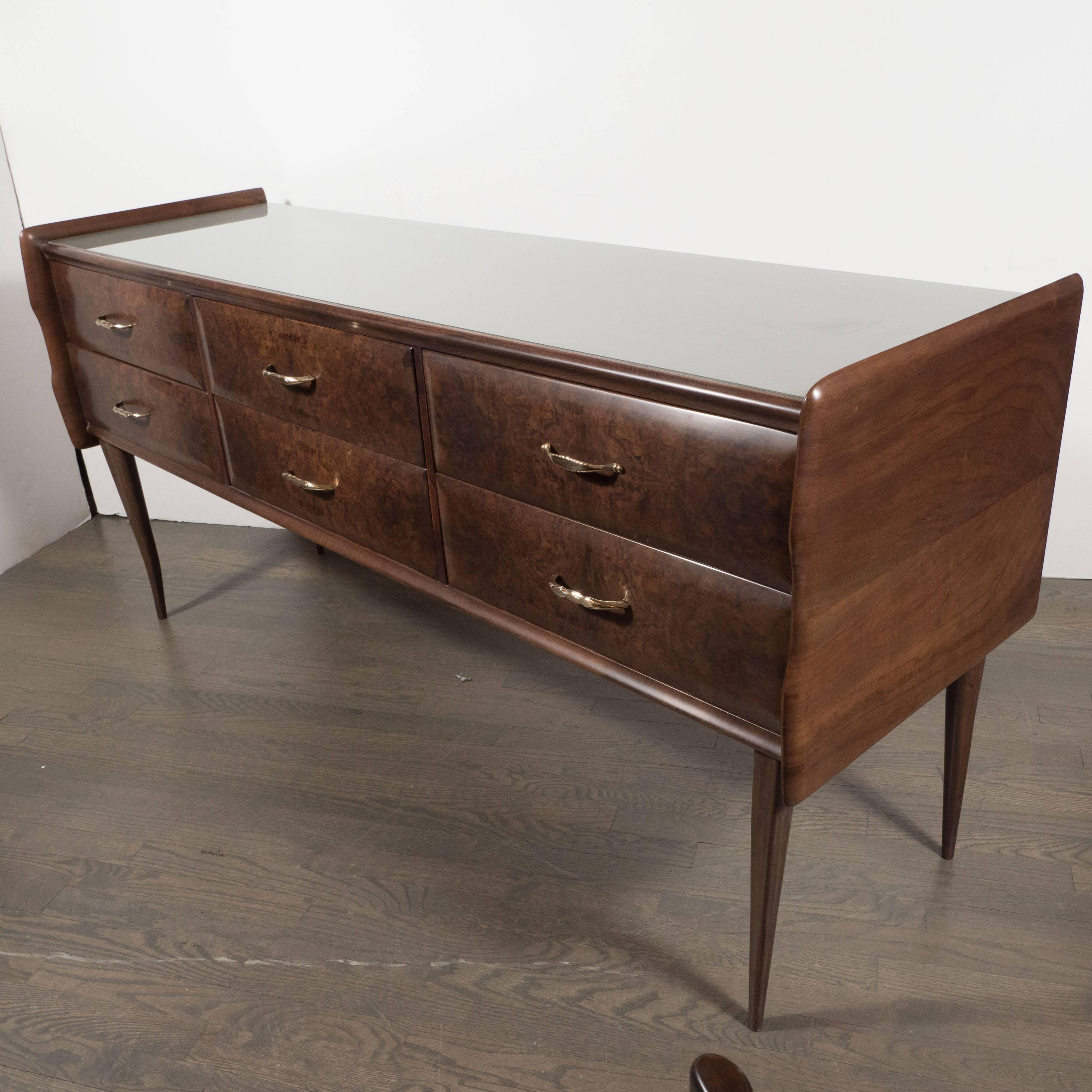 This stunning Mid-Century Modern chest was realized, in the Manner of Gio Ponti, in Italy, circa 1950. It has been handcrafted in burled and hand rubbed book matched walnut, with stylized demilune brass pulls and a black vitrolite top. No aesthetic