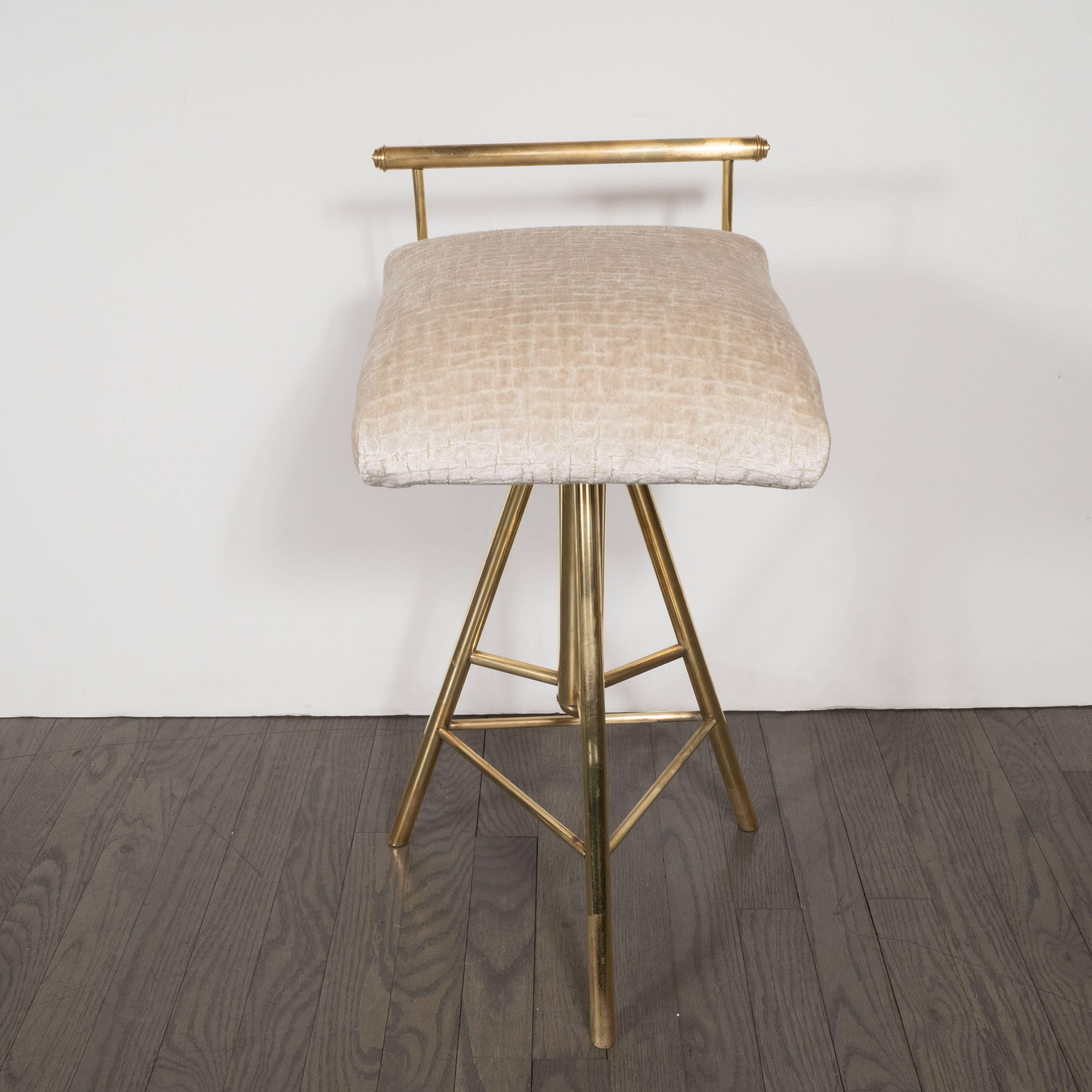 This stunning Mid-Century Modern stool features a tripod form consisting of three cylindrical brushed brass legs connected with triangular supports. The swiveling seat attaches to a circular base from which extends a cylindrical rod that connects to