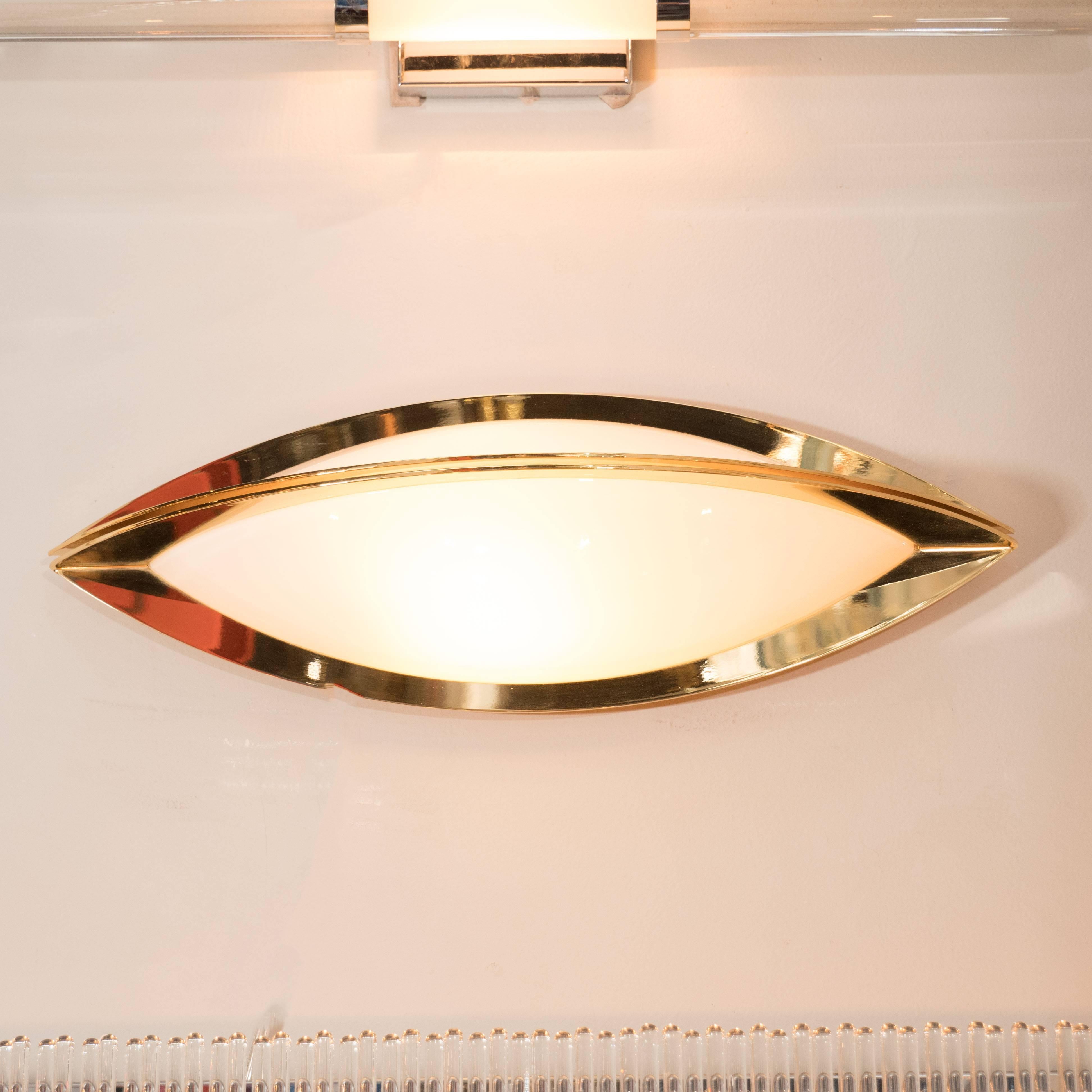 This sophisticated vanity sconce was realized by the esteemed German lighting studio Glashütte Limburg in Germany, circa 1960. It features an ovoid form consisting of two polished brass demilunes that meet culminate in the center, coming within