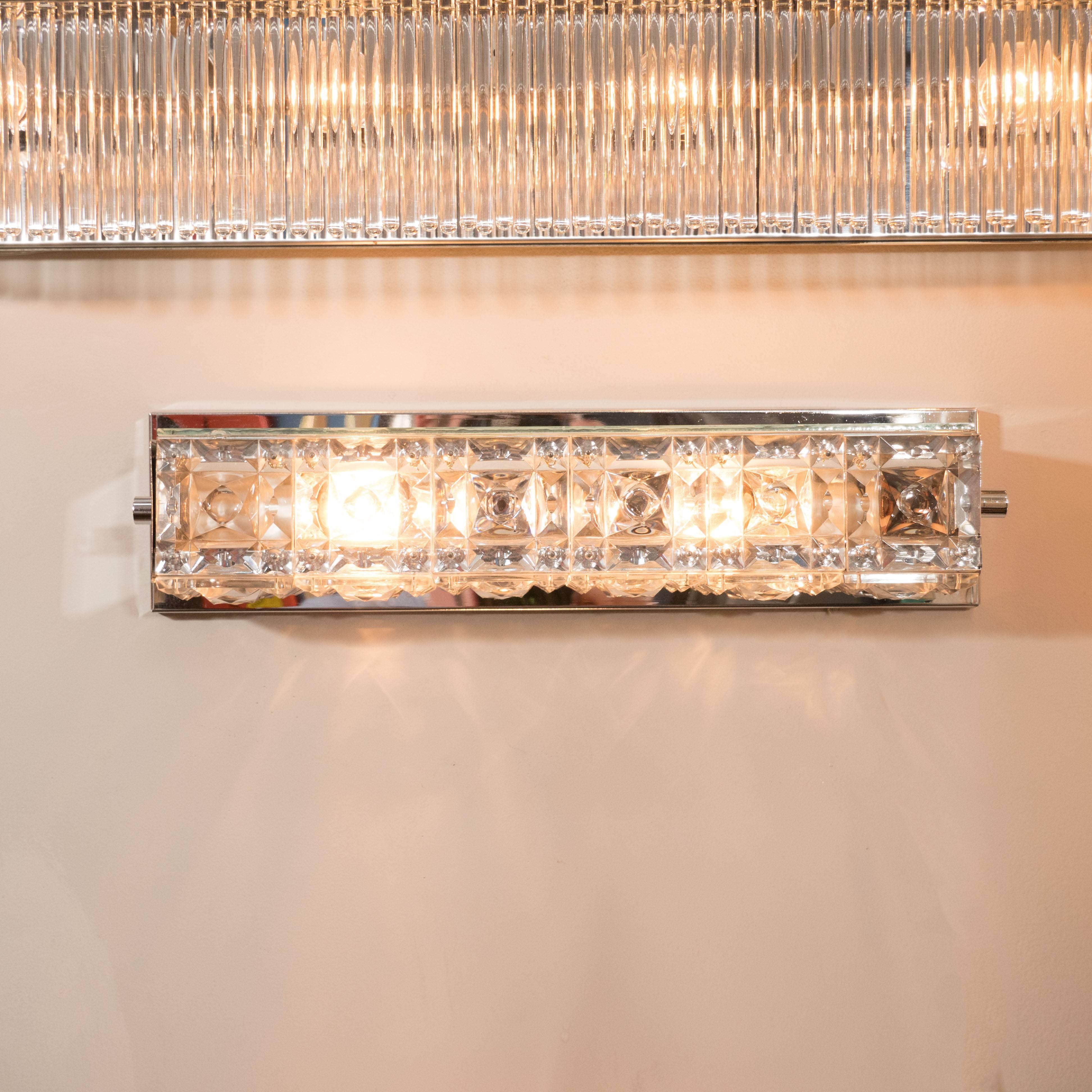 Created by the renowned Austrian atelier J.T. Kalmar, exquisite rectangular sconce features a cut crystal face- resembling diamonds set in a platinum band- with square chrome sides each offering a cylindrical embellishment in their center. This