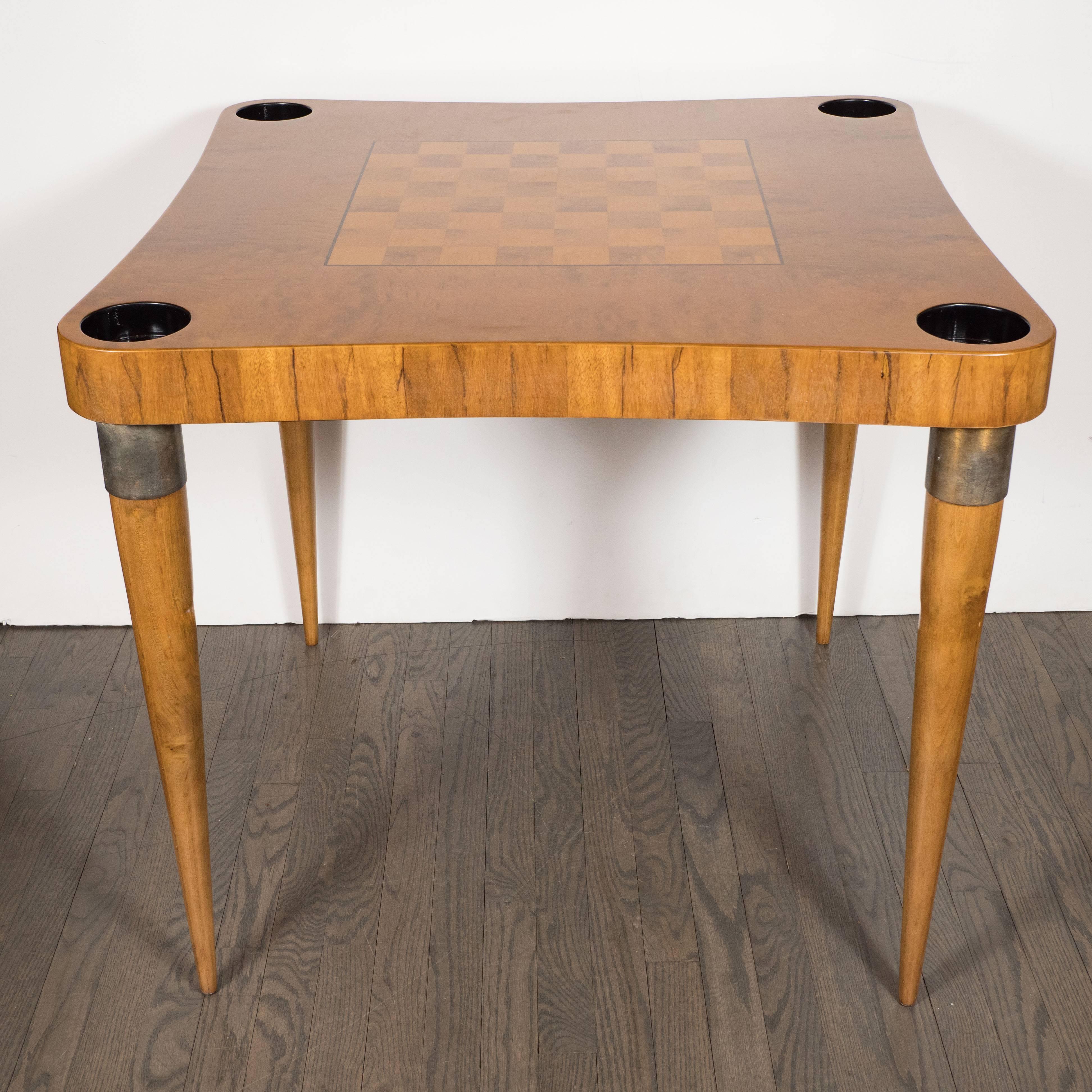 This elegant game table was realized by Gilbert Rohde- one of the most celebrated American designers of the 20th century- circa 1939. It features conical legs with antique brass wrapped details at their top; an inlaid chess board realized from white