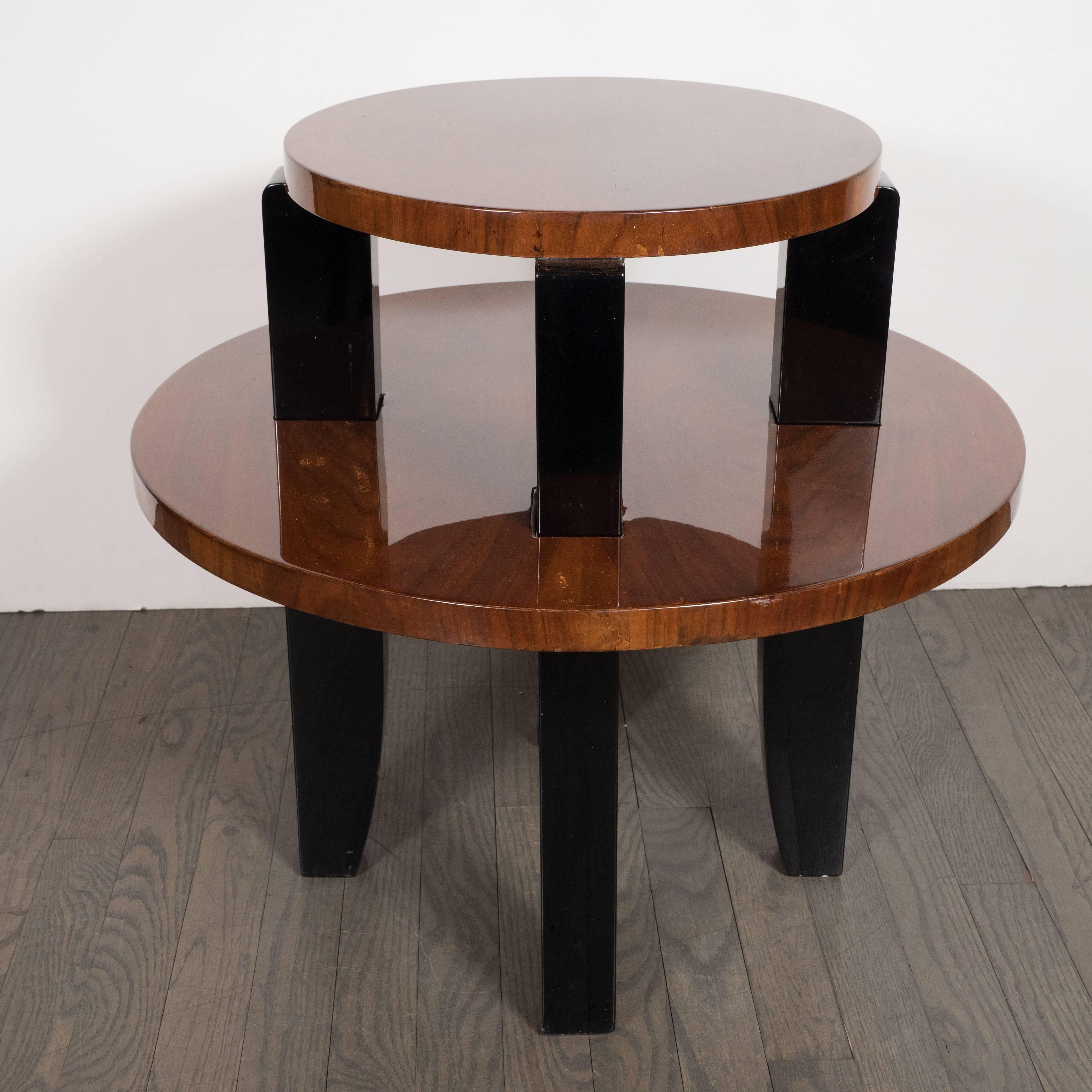 This stunning two-tier occasional/ side table was realized in France, circa 1935. It features two circular tiers composed of bookmatched walnut attached with black lacquer saber style legs. This piece showcases the understated and refined beauty of