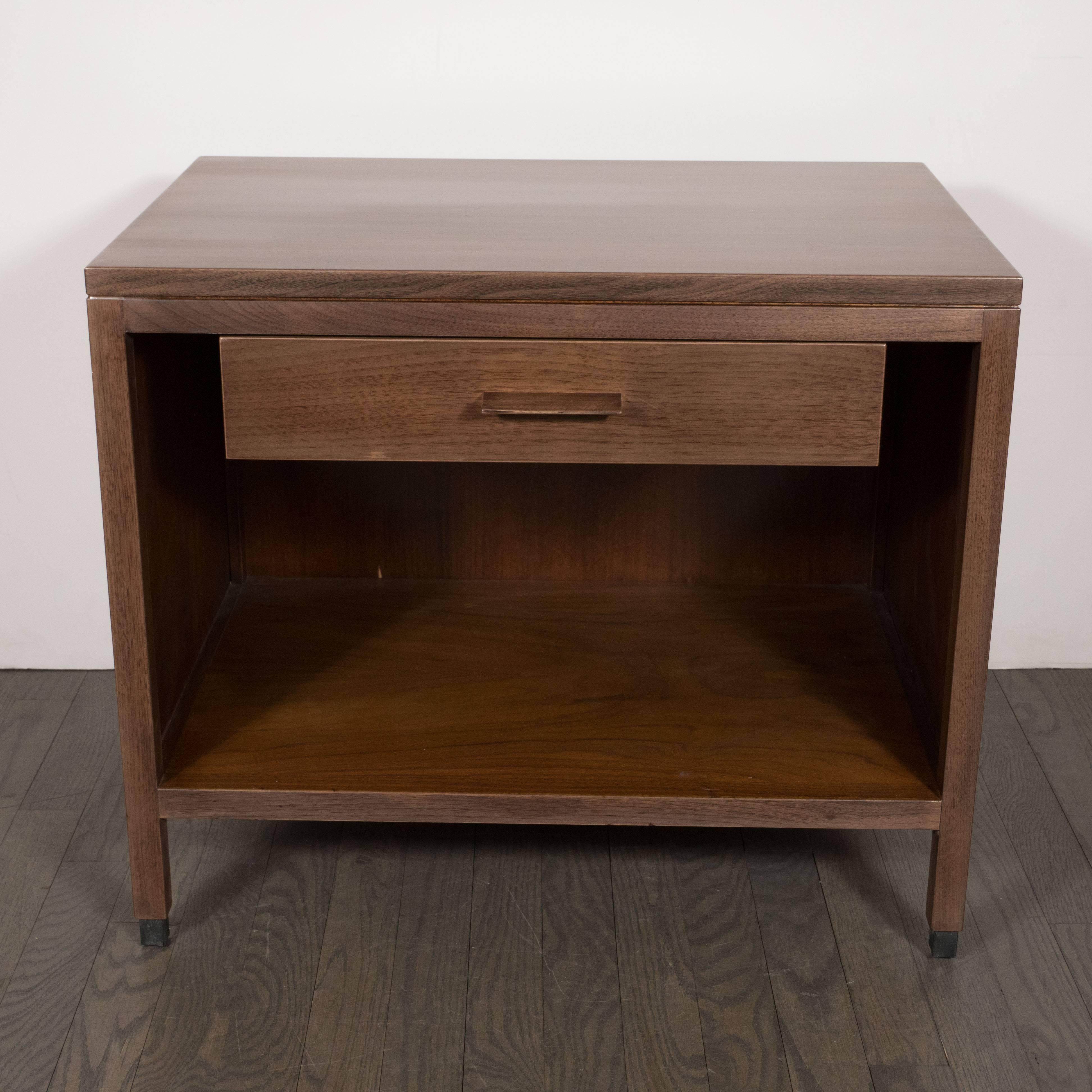 This pair of sophisticated Mid-Century Modern end tables or nightstands were realized in the United States, circa 1950. Realized from hand rubbed and bookmatched walnut with cane side panels and square skyscraper style black lacquer feet, they