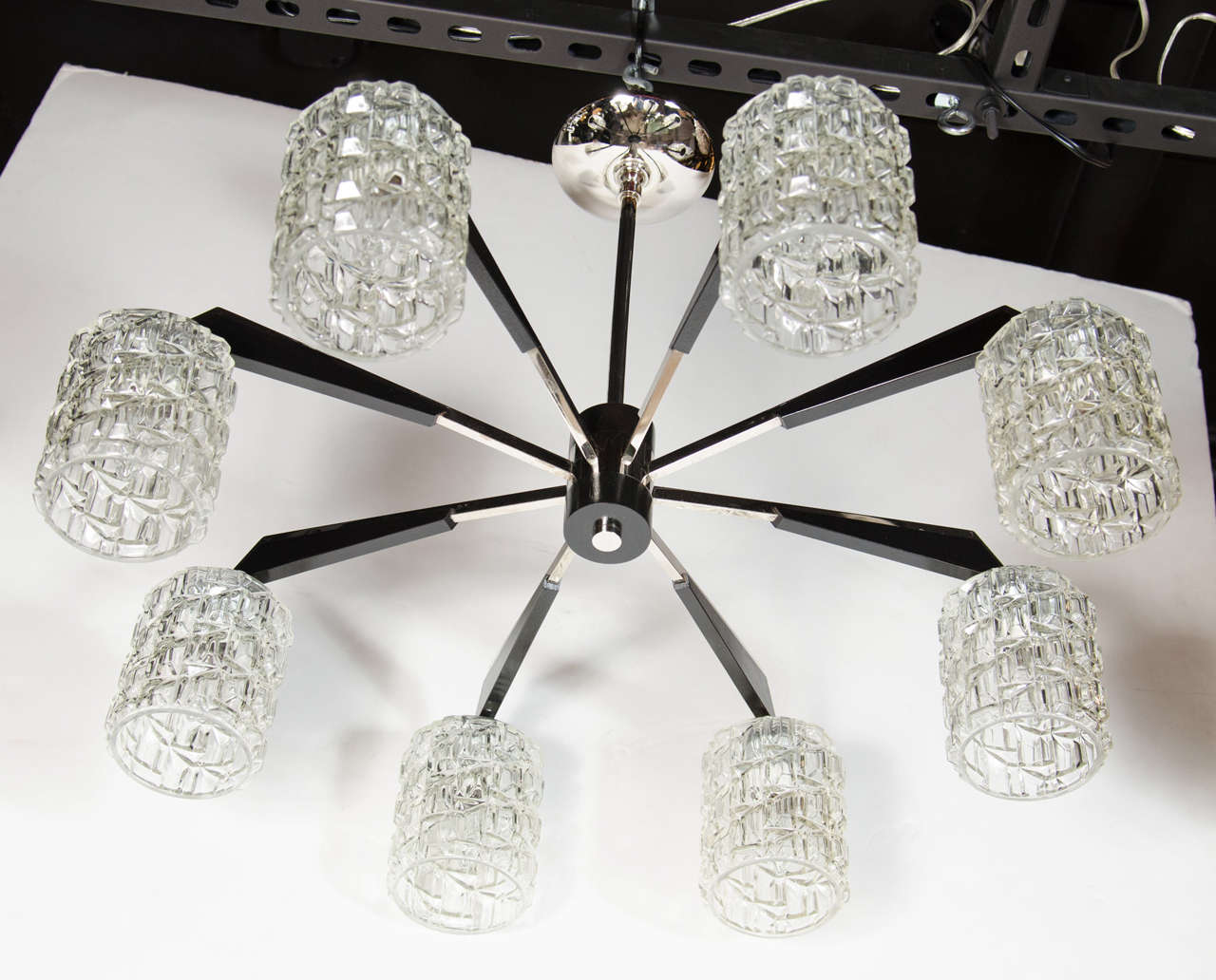 This graphic Mid-Century Modern chandelier was realized in Denmark, circa 1960. It offers eight-arms emanating from a cylindrical body in ebonized walnut with a chrome finial of the same shape adorning its base. The chrome arms have geometric