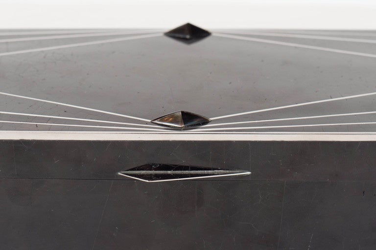 This exquisite black tab shell lidded box features a rectangular shape with a silvered inlay lineal Art Deco diamond design with a raised and faceted mother-of-pearl detail and silvered angular handle on the lid. The interior is lined with black