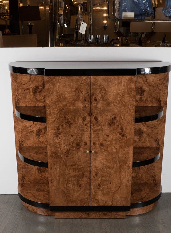 A stunning Art Deco bar cabinet in exotic book-matched Walnut with black lacquer banding details.  This exquisite Art Deco bar features a two door front of exotic book-matched Walnut with brass handles that opens up to a fully open cabinet with an