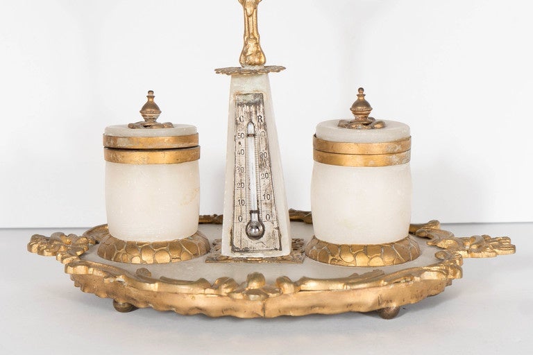 This elegant 19th century ormolu bronze and white Carrara marble writing desk fitted with two inkwells and an antique mercury thermometer. This recherche object from the mid-19th century features an oval shaped based with a scrolling and stylized