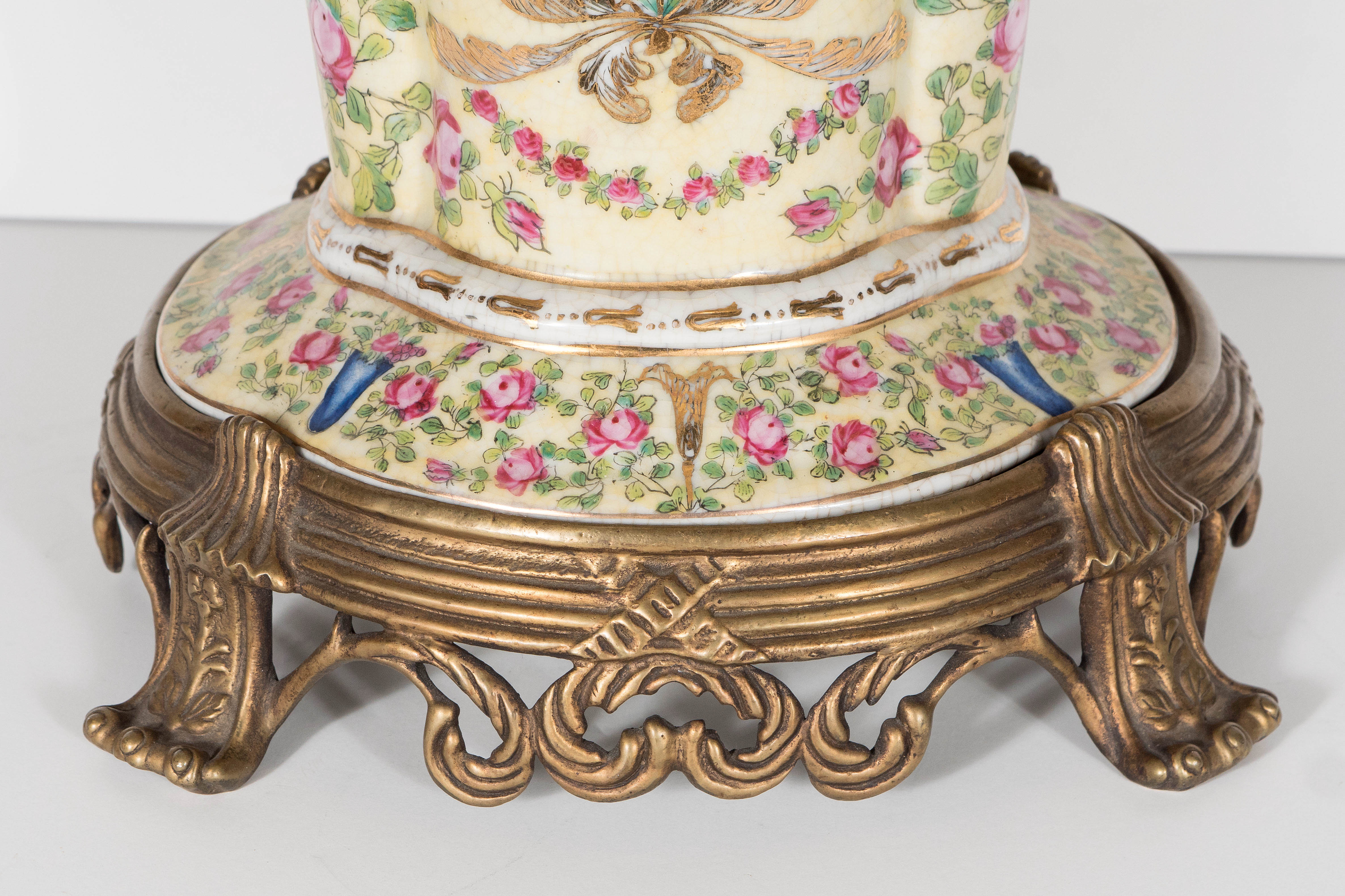 This stunning porcelain vase by United Wilson Co. features hand-painted climbing roses, gilded palm fronds and a sapphire blue urn in the centre of the composition. The vase rests on a brass pedestal with scrolling Baroque detailing. This stunning