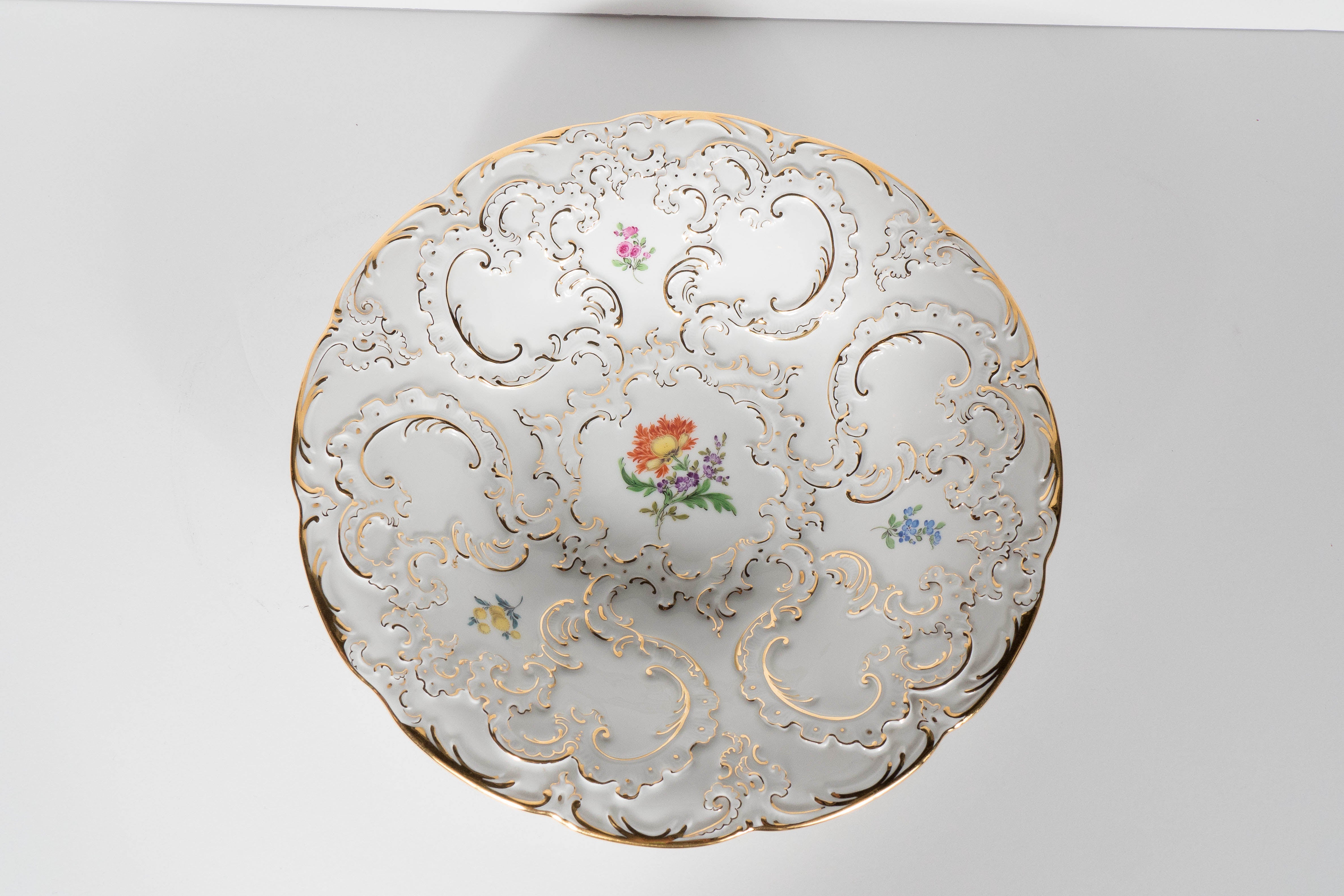 This porcelain bowl features exquisite Baroque-Style relief detailing with accents of 24 carat yellow gold and hand-painted floral design. A gorgeous accessory that can be used in a multitude of ways. This piece is in mint condition. This bowl bears