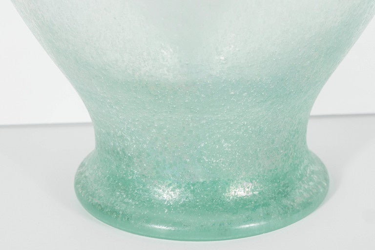 This large hand blown vase /urn features a pale iridescent celadon green glass with a scavo finish.It features a scrolled arm design. This is a stunning piece that will make a great impact wherever it is used.