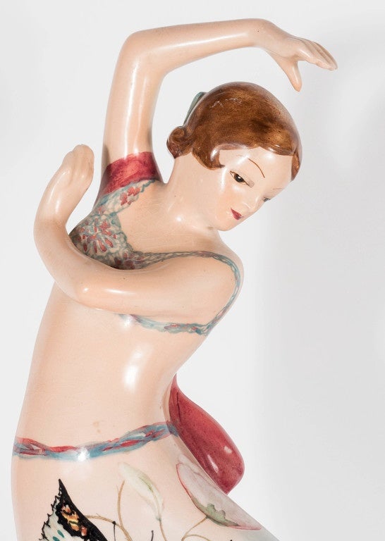 This ceramic hand-painted figurine portrays a female dancer in mid-move and depicted in a pastel dress with a Peonies background and a large butterfly in the foreground. Her skirt has an ombre effect that starts in Celadon then finishes with a peach