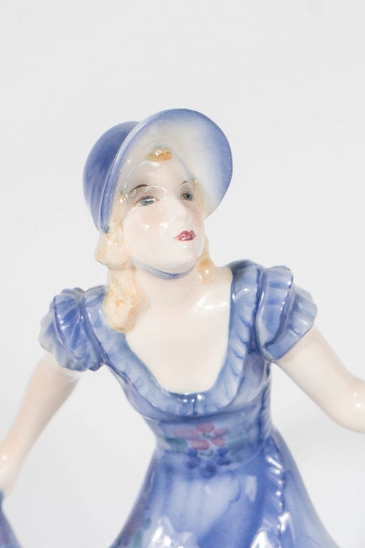 This ceramic figurine of an elegant woman portrayed in a hand-painted gown of Lilac coloring with highlights of white hues is named 'Congress, Lilian Harvey'. Her gown is of a beautiful Lilac color with a ruffled trim that features bouquets of