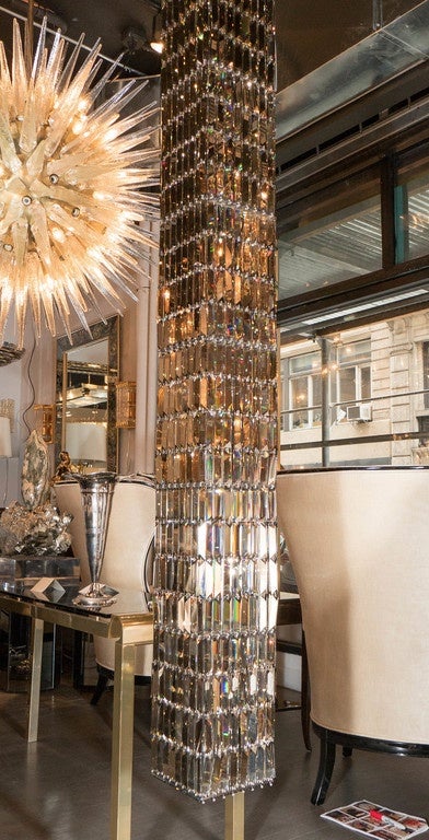 This magnificent chandelier designed by George Beadle for Swarovski, titled 'Glitterbox,' is a true work of art with its towering column-like design that is comprised of Swarovski crystal prisms in the crystal golden teak color way. The interior of