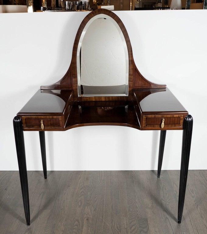 This gorgeous vanity features a fluted and tapered leg design. It is made of rosewood, walnut and ebony and accented with black lacquer with stylized brass pulls and an arched beveled mirror. The book matching and inlay detailing on this piece is