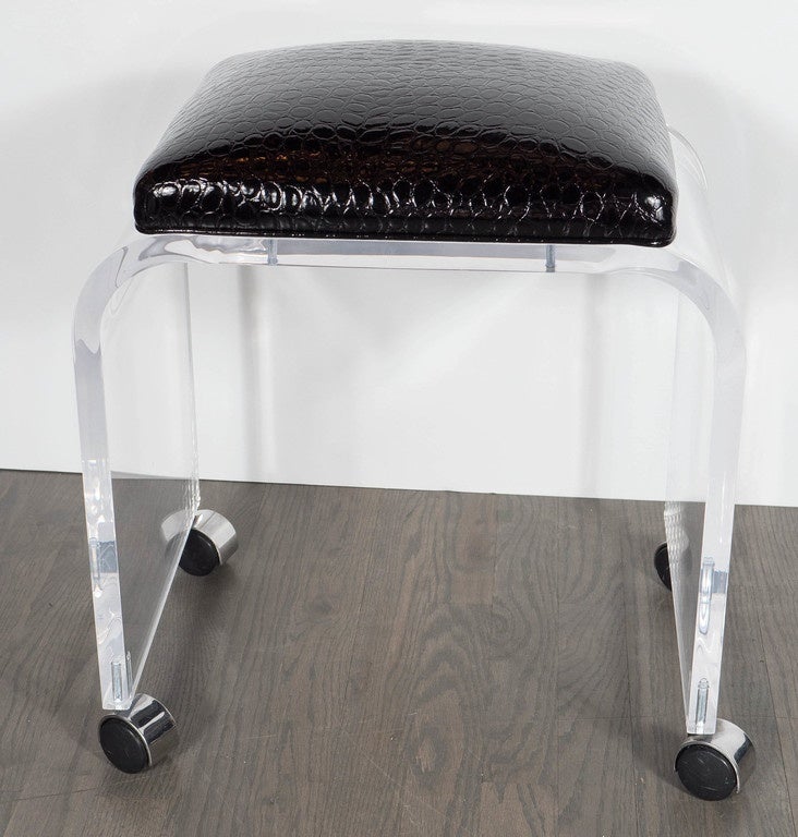 This bench or stool features a thick Lucite design with a waterfall design newly upholstered in a faux black crocodile. It rests on castors which would make it really great as a vanity stool. This piece has been newly upholstered.