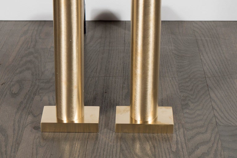 These stunning pair of custom andirons were designed and realized exclusively for High Style Deco. They feature brushed brass cylindrical form bodies with black enamel supports. Hand crafted by artisans, these andirons offer clean modernist lines