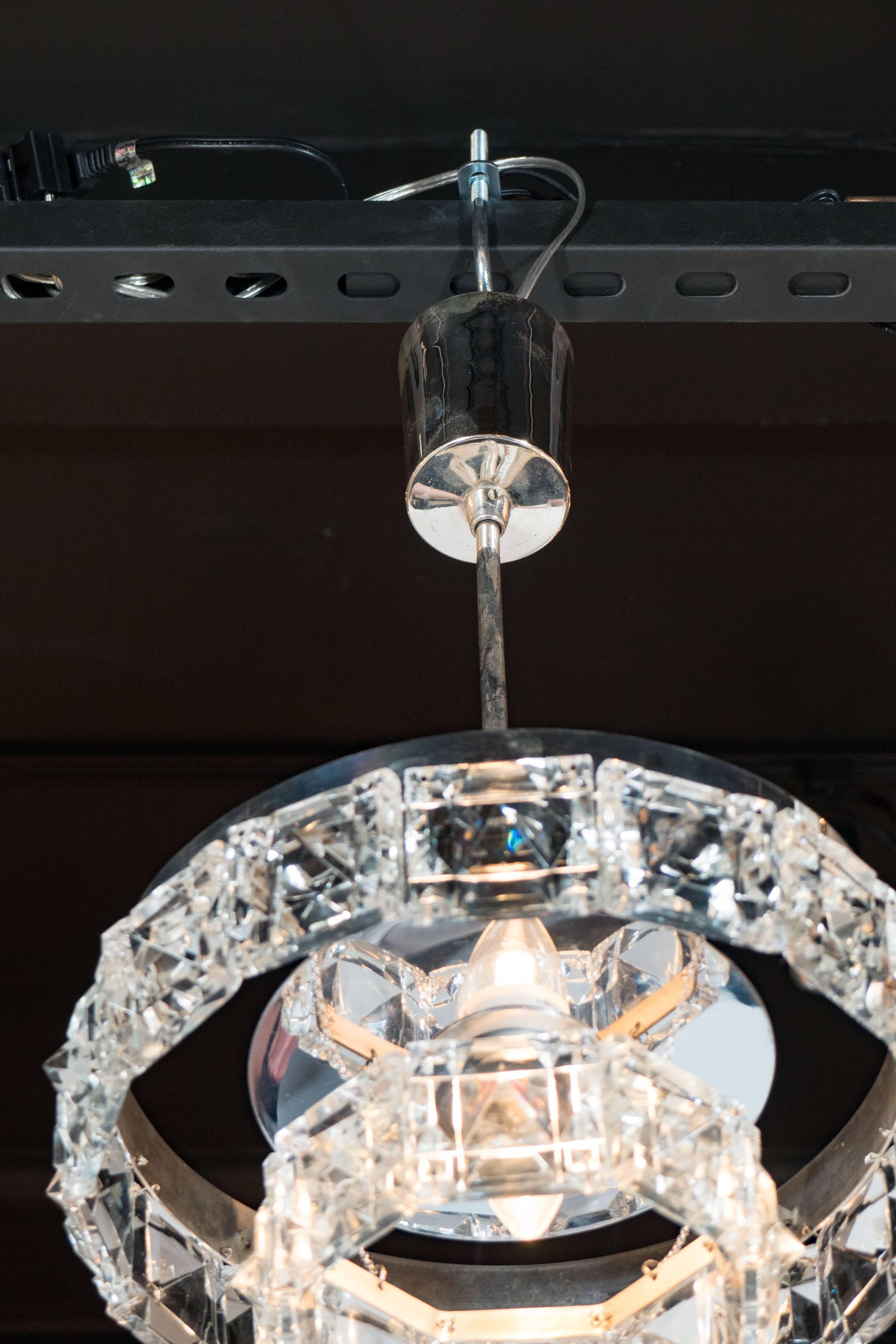 Ein eleganter, zweistufiger Kristallkronleuchter mit Chrombeschlägen von Kinkeldey aus der Jahrhundertmitte. Handgeschliffene, facettierte, quadratische Kristallsegmente sind auf zwei absteigenden Ebenen aneinandergereiht. Ein poliertes Chromband